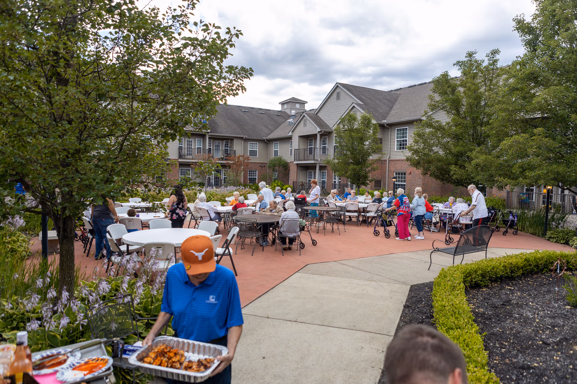 Outdoor courtyard at Assisting Hands Home Care with residents seated at tables and staff serving.