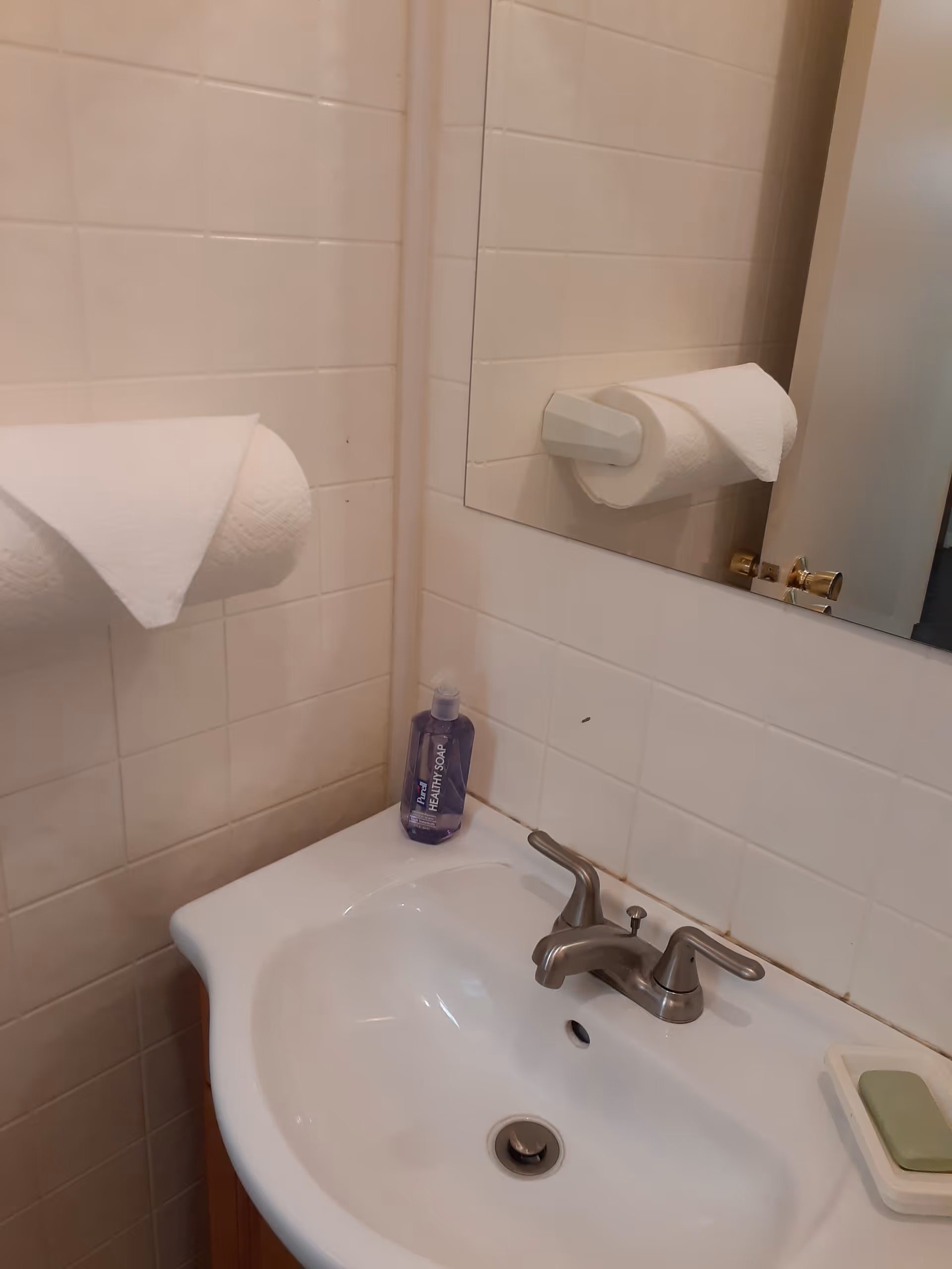 Tiled bathroom sink with faucet, mirror, towel, and soap dispenser.