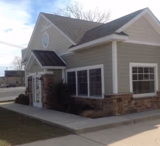 Single-story building exterior with beige siding, stone accents, and a front entrance.
