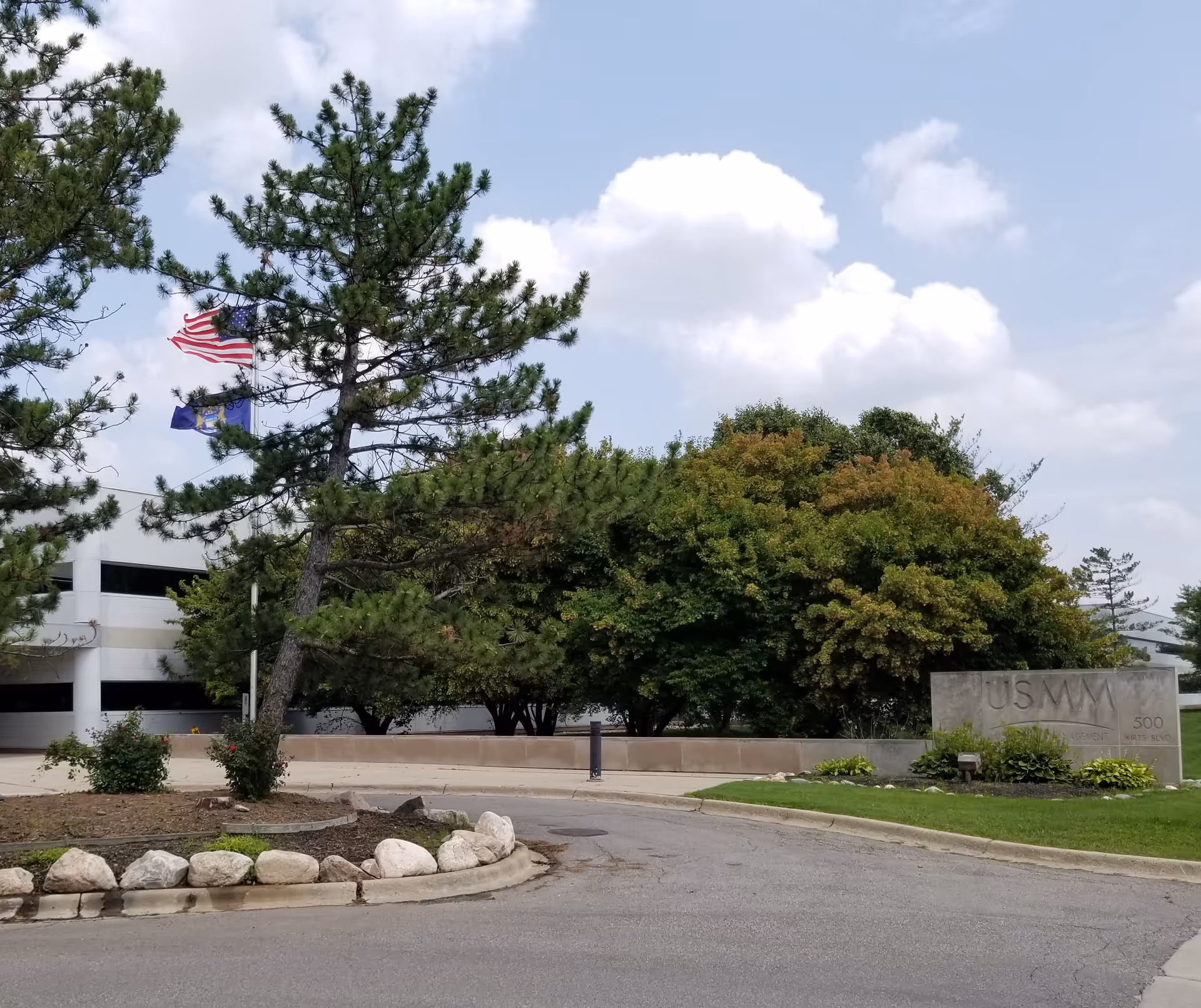 Outdoor view of HarmonyCares facility with flags, trees, and a stone entrance sign.