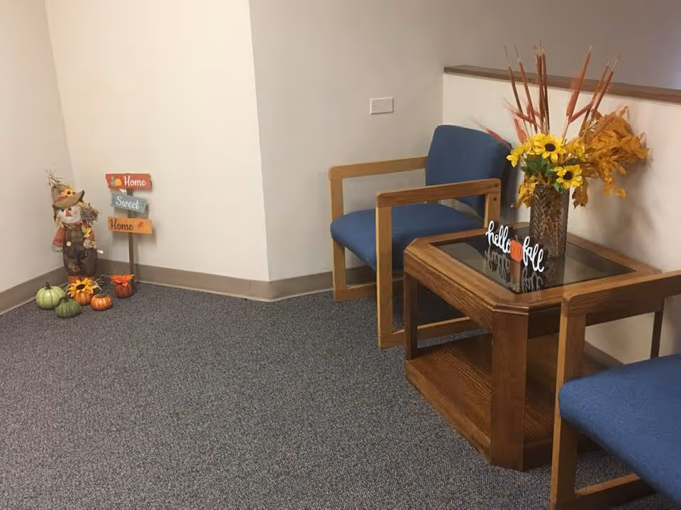 Interior waiting area with blue chairs, autumn decor, and a vase of flowers.