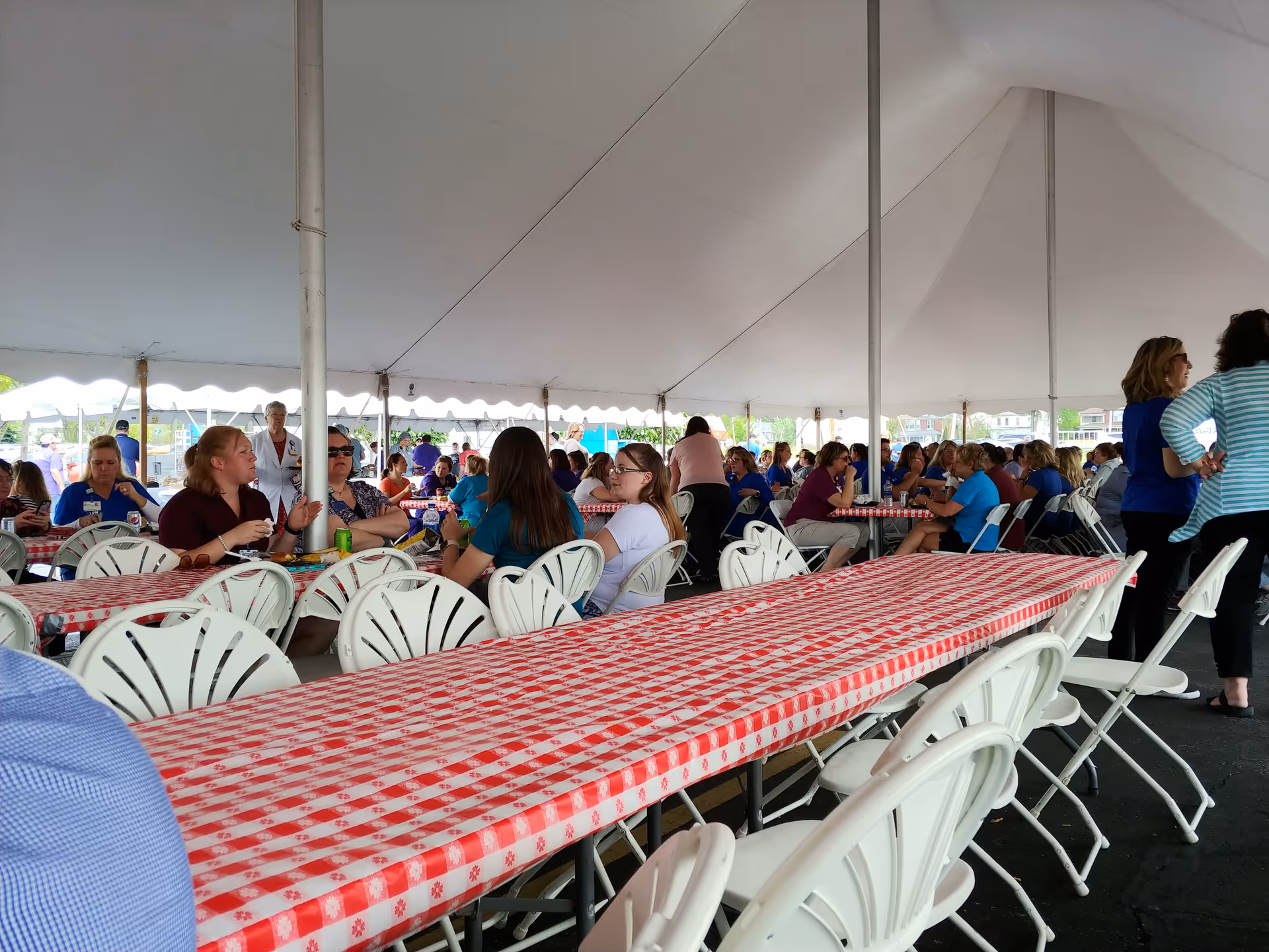 Large outdoor tent with long rows of checkered tables and many people dining.