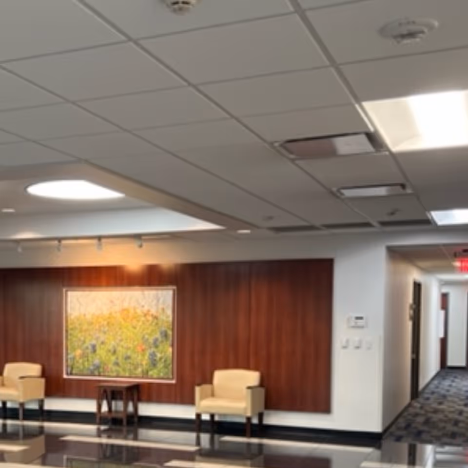 Lobby area with wood-paneled wall, framed artwork, and beige chairs.