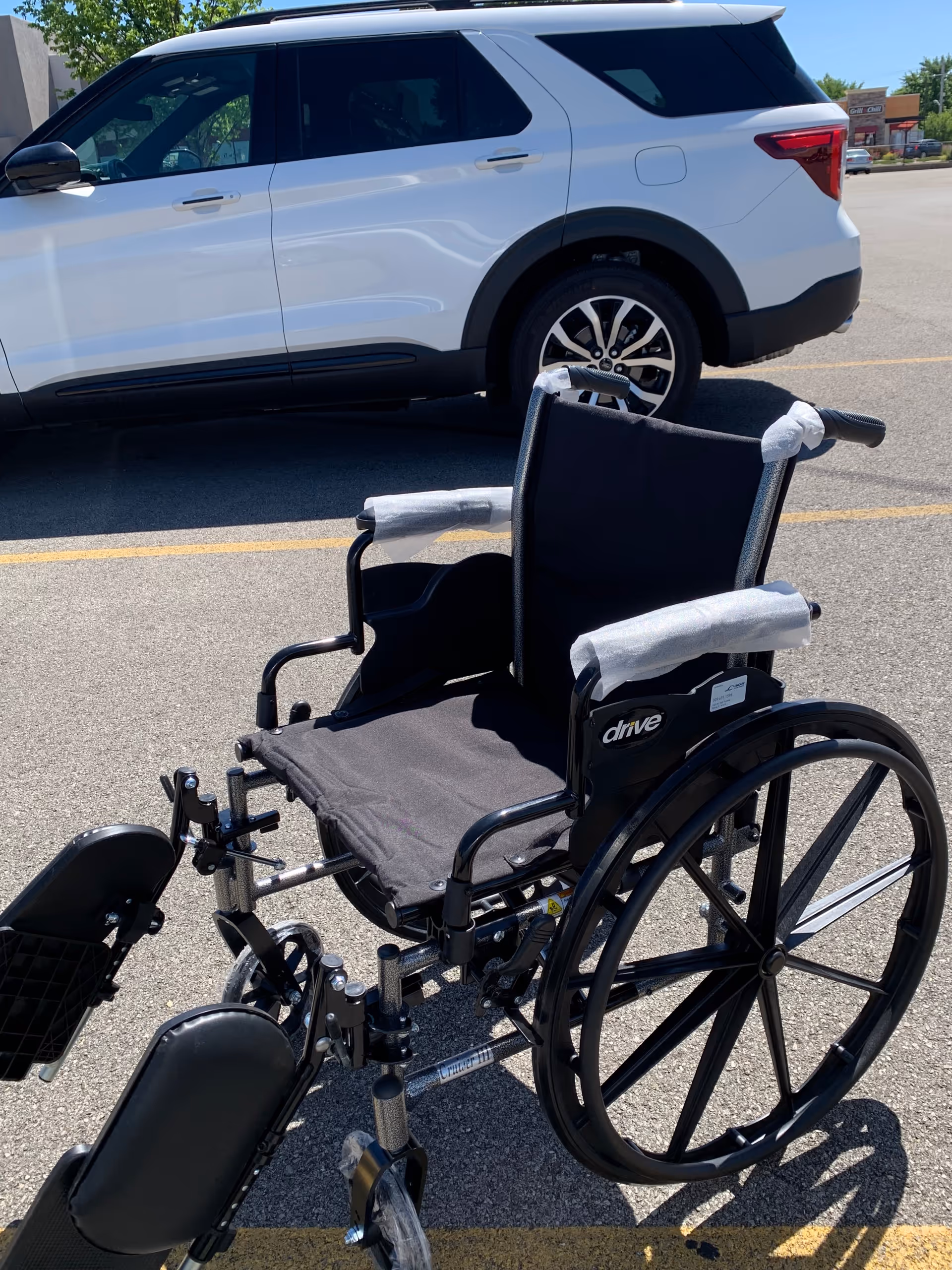 Wheelchair in a parking lot beside a white SUV outside a facility.