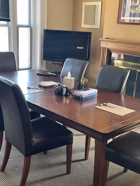 Interior conference-style room featuring a large wooden table, black chairs, TV, tissue box, and fireplace.