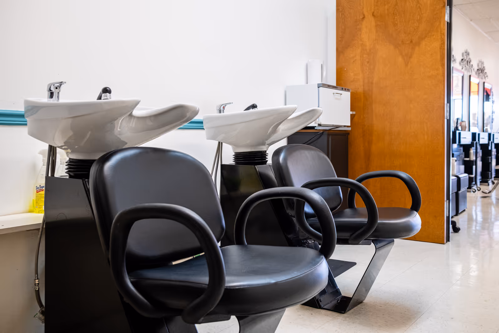 Row of black salon chairs with white washing basins in a senior living facility.
