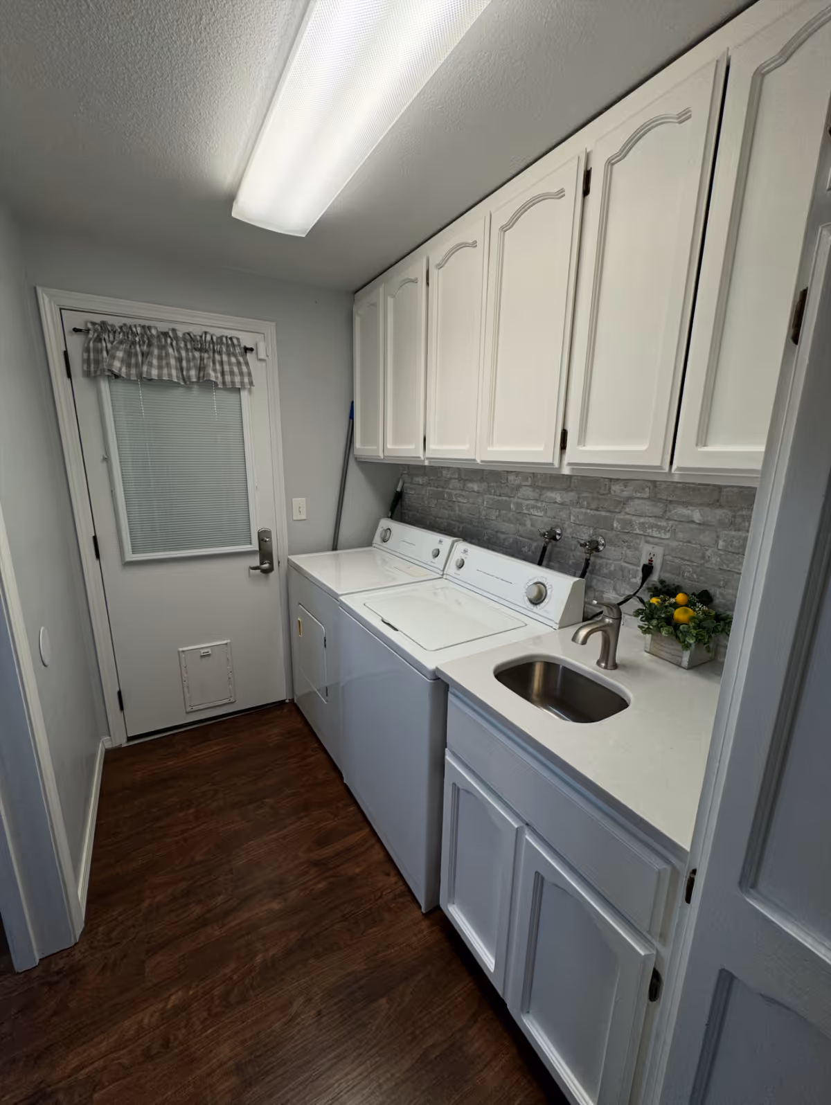 Utility laundry room with washer, dryer, sink, and white cabinets.