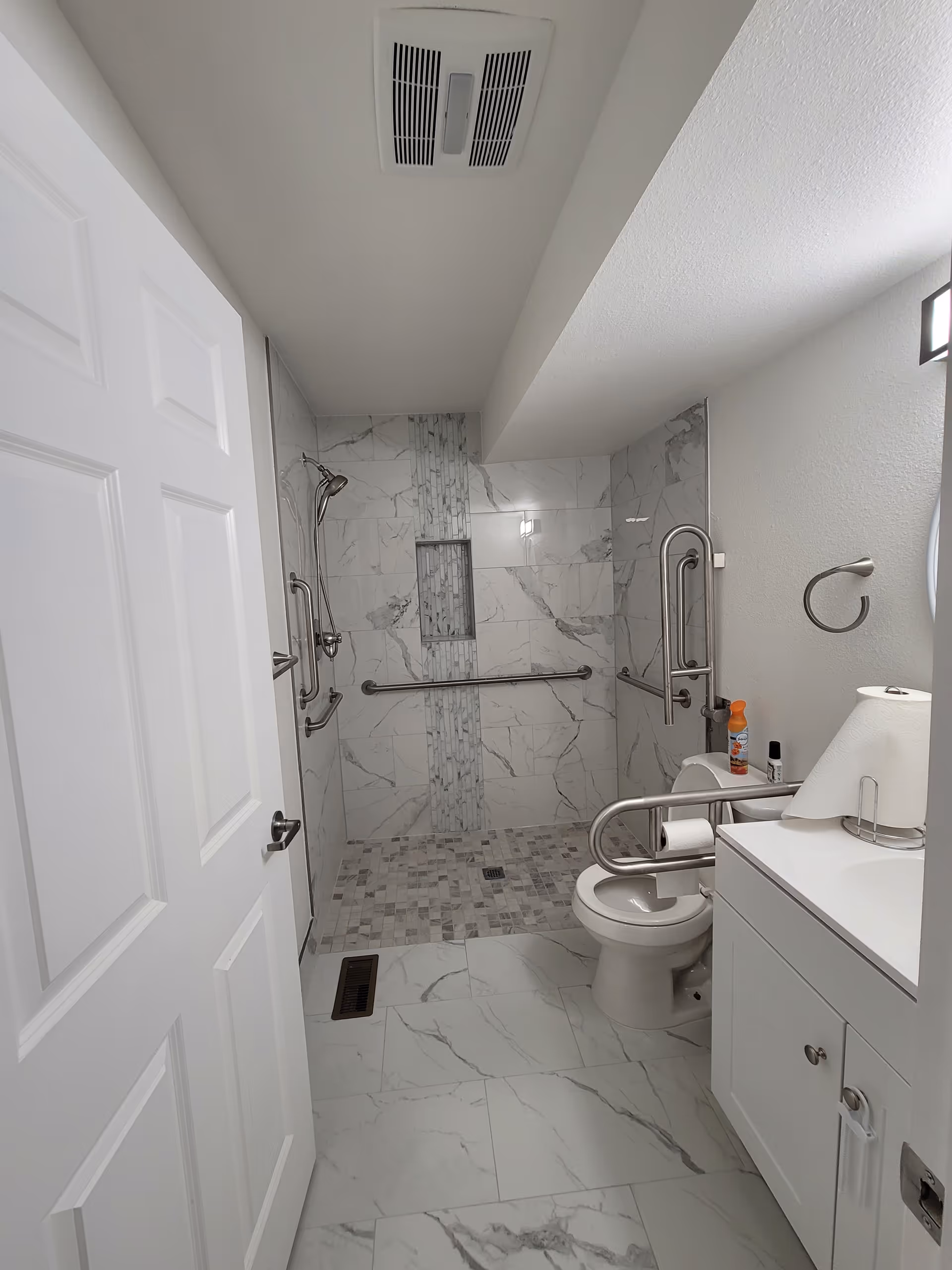 Accessible bathroom with tiled shower, grab bars, toilet, and sink in a senior living unit.
