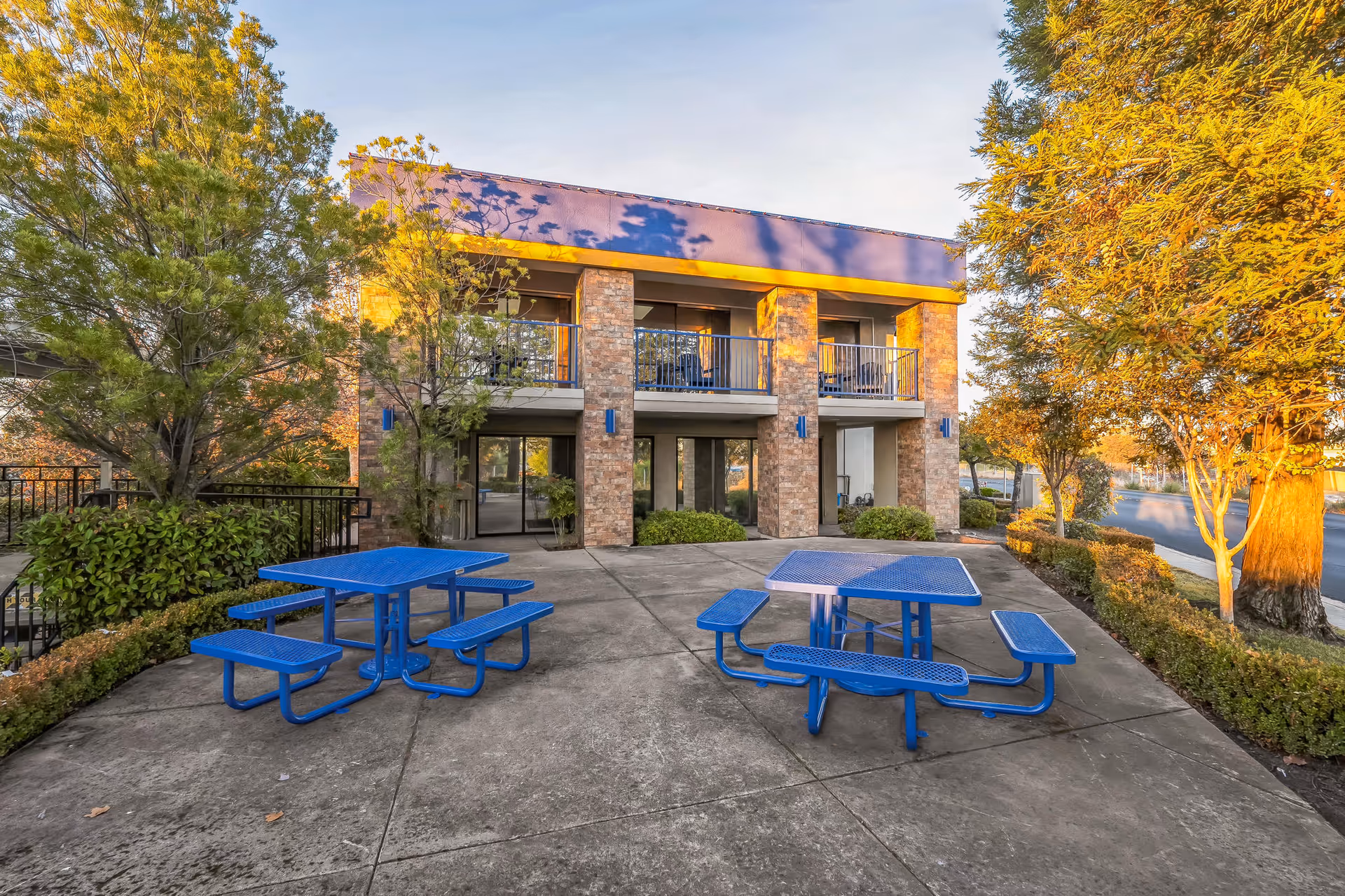 Outdoor concrete patio with blue picnic tables in front of a brick senior facility.