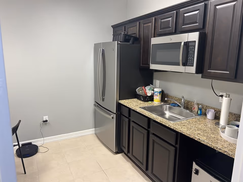 Modern kitchen with stainless steel fridge, microwave, granite countertops, sink, and dark cabinets.