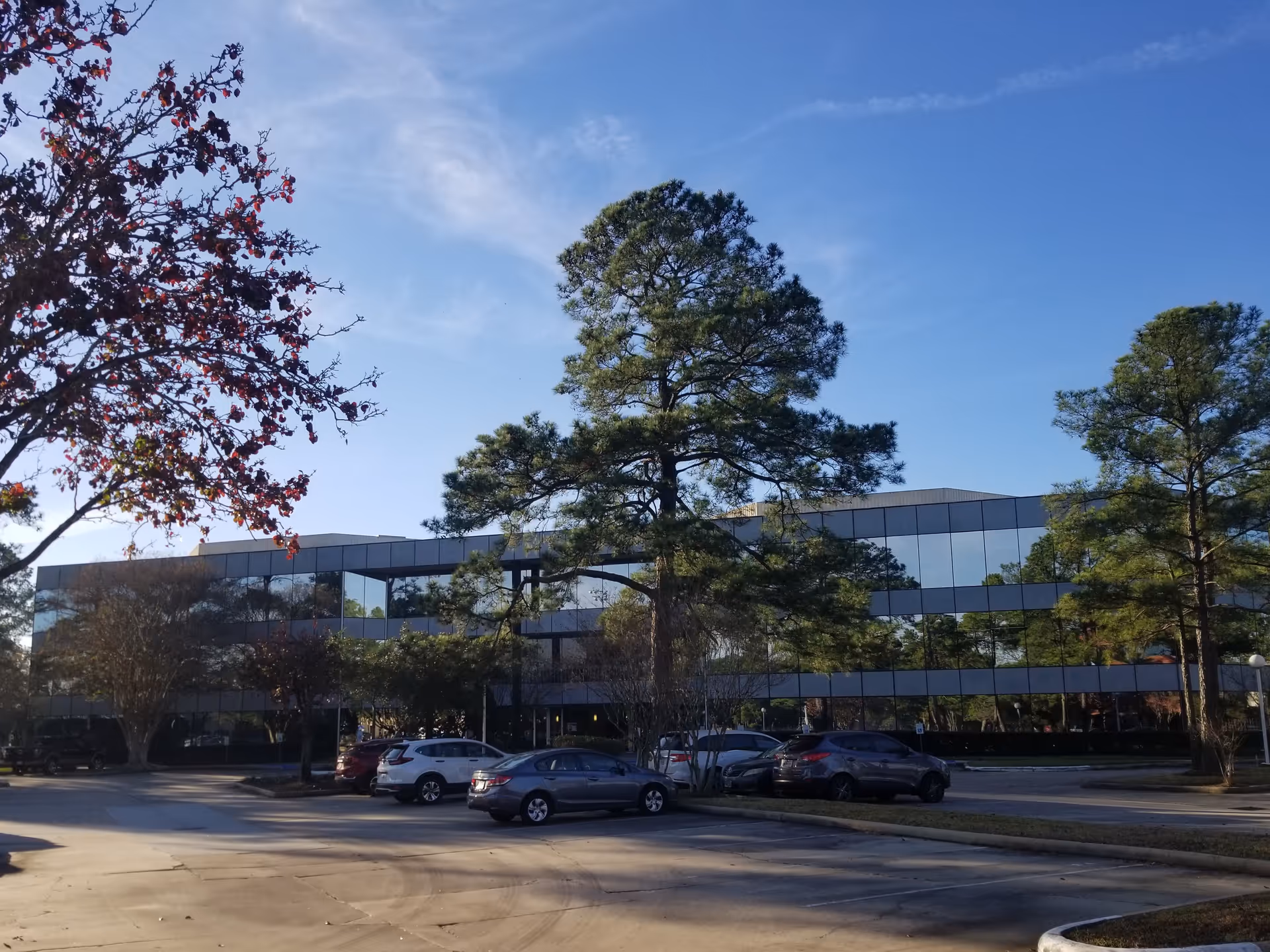 Modern glass-front senior living building with parking and trees