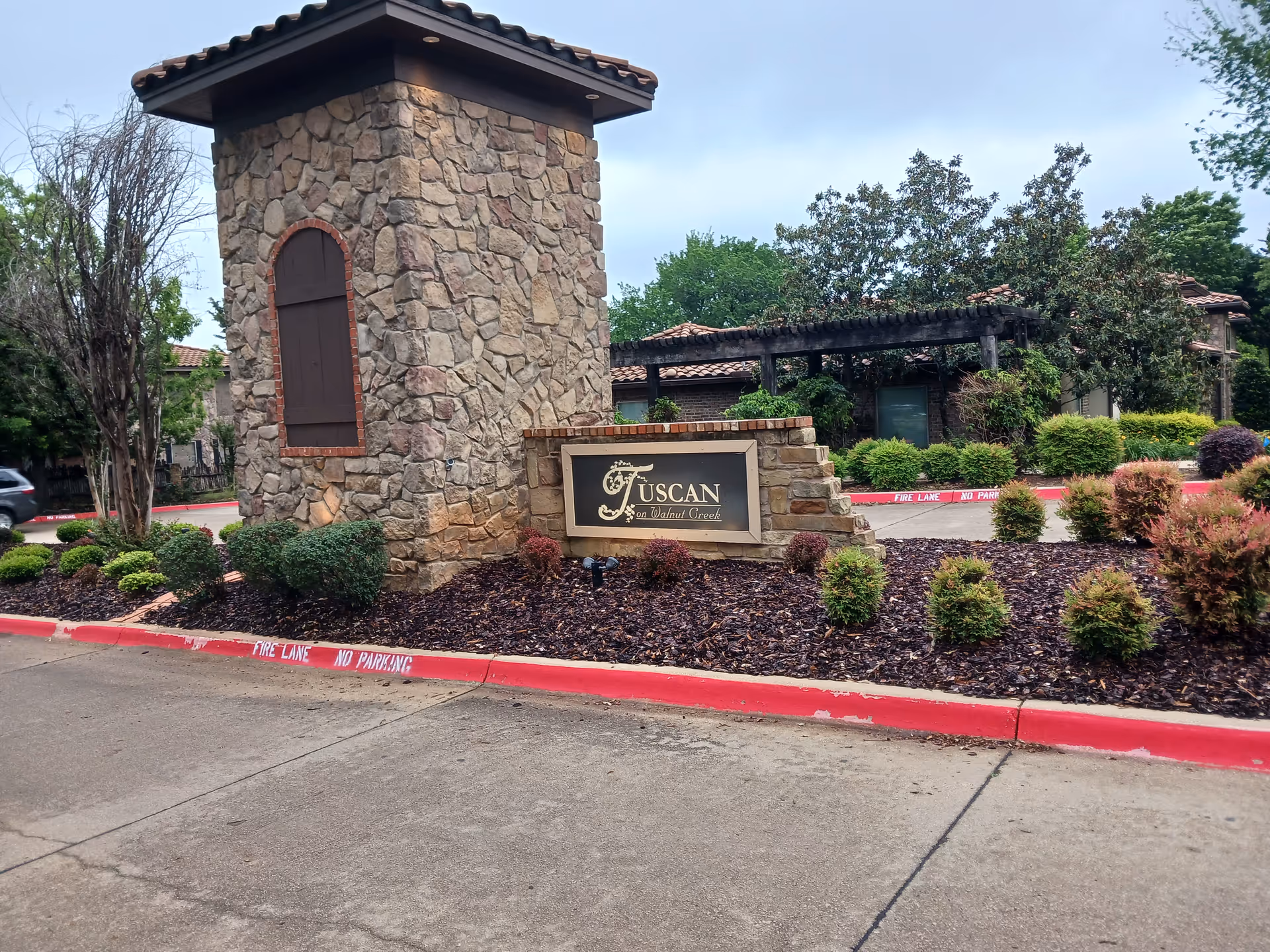 Stone tower and Tuscan-style sign greet the landscaped entrance of a senior living community.