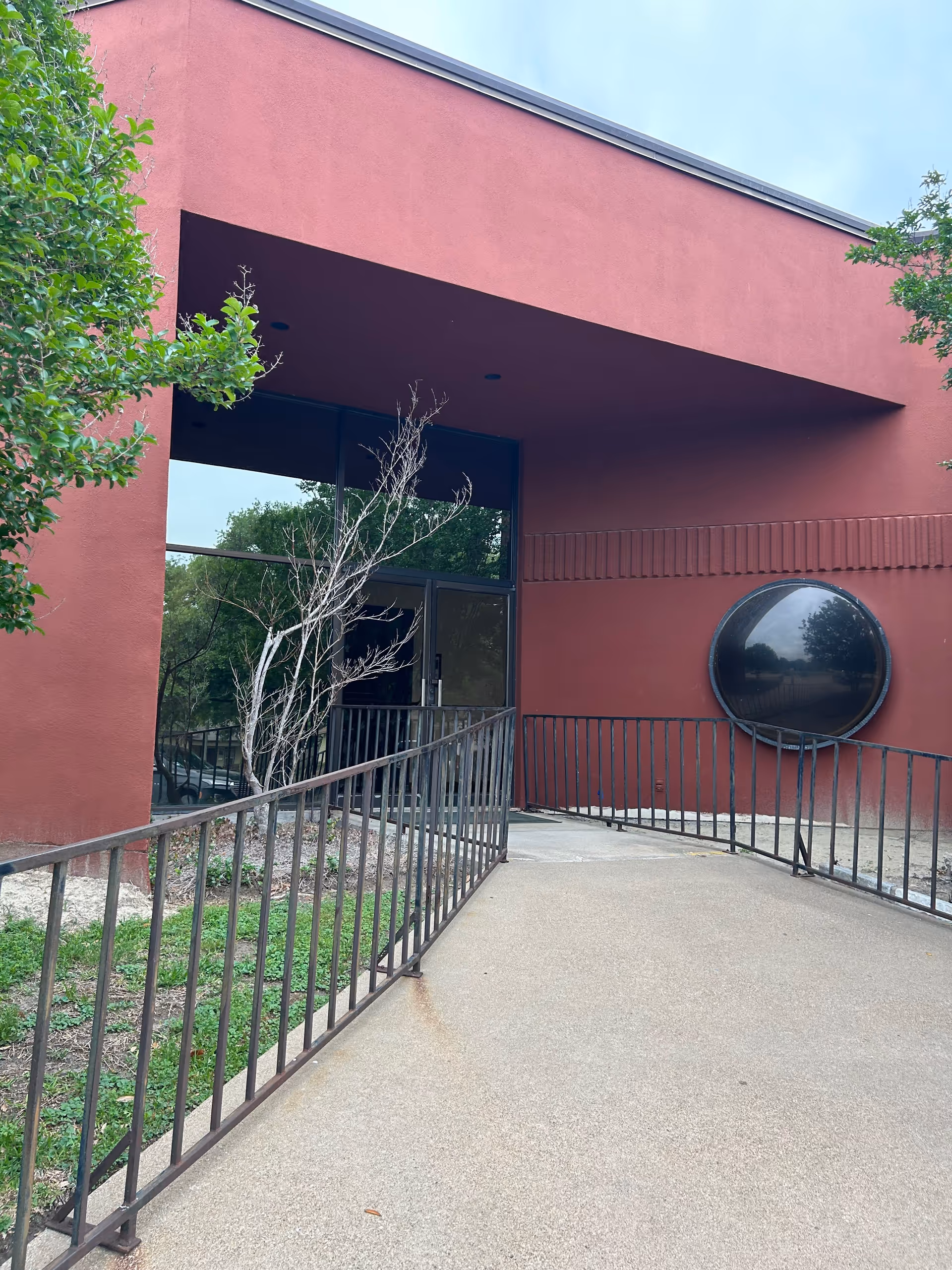 Exterior view of a red senior living facility entrance with ramp and railing.