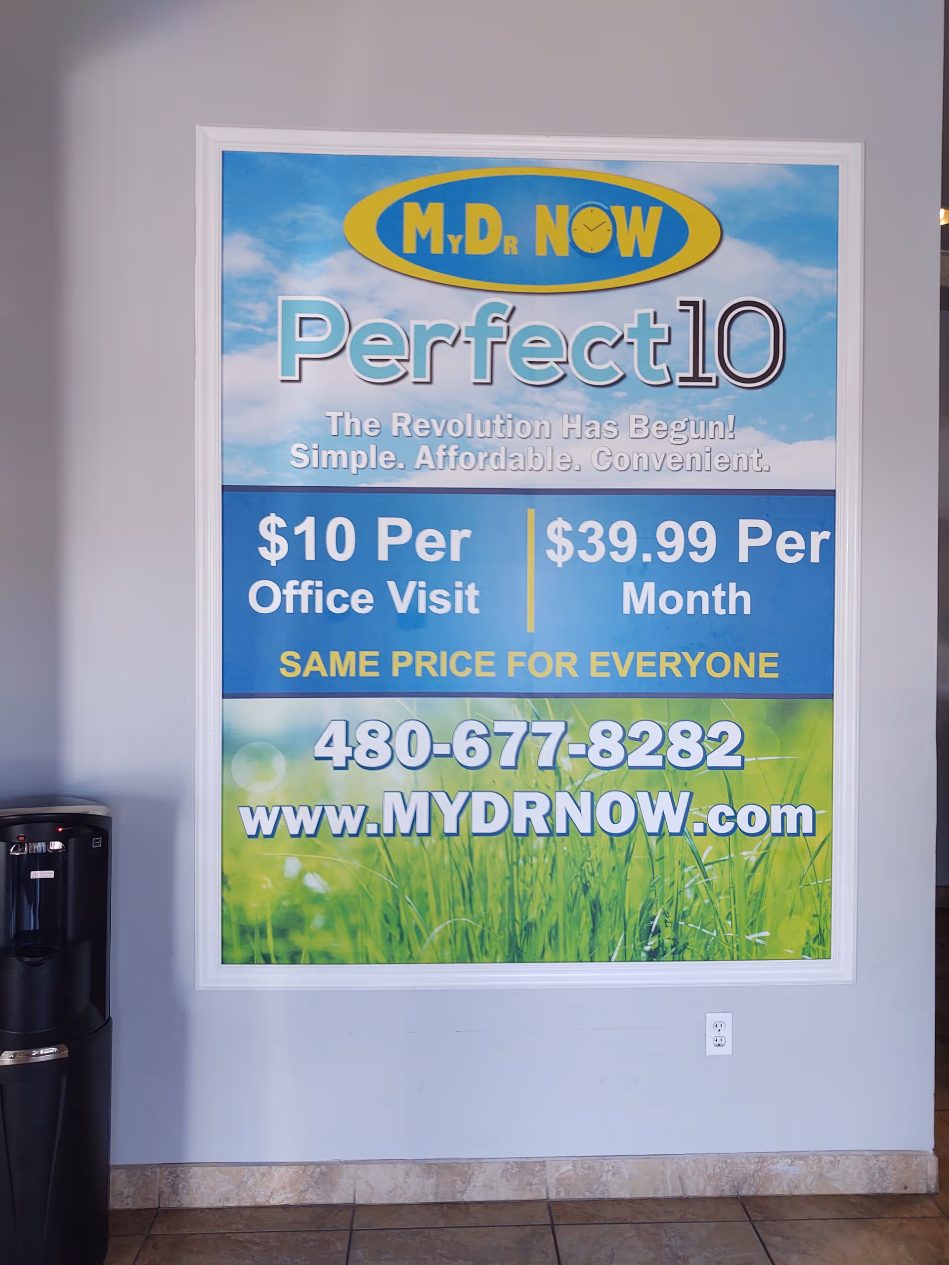 Inside a facility lobby, a MY DR NOW poster on a gray wall near water cooler.