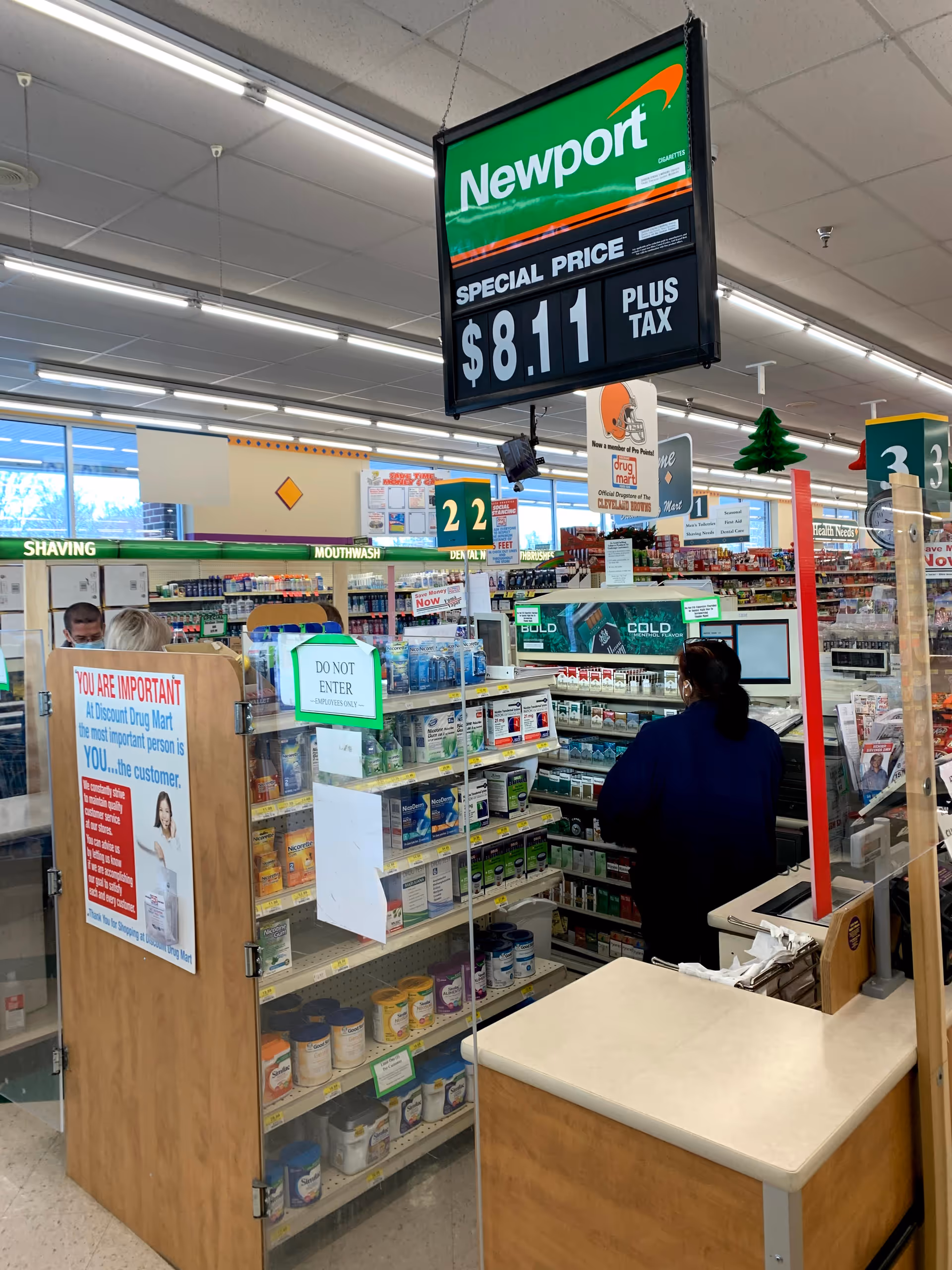 Inside a Discount Drug Mart pharmacy with shelves, a customer, and bright overhead lighting.