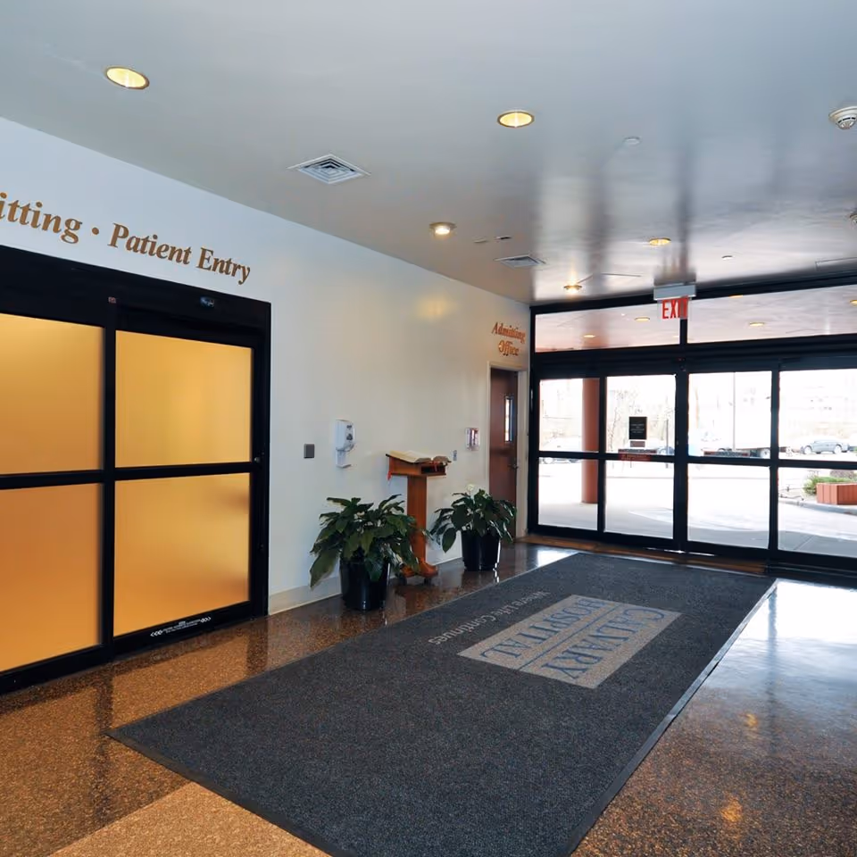 Calvary Hospital lobby with glass doors, potted plants, and an admissions desk.