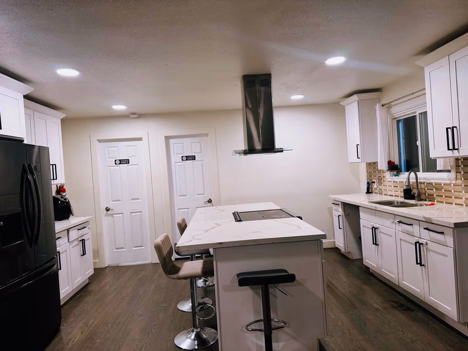 A modern white kitchen with an island, cabinets, stainless steel appliances, and a range hood.