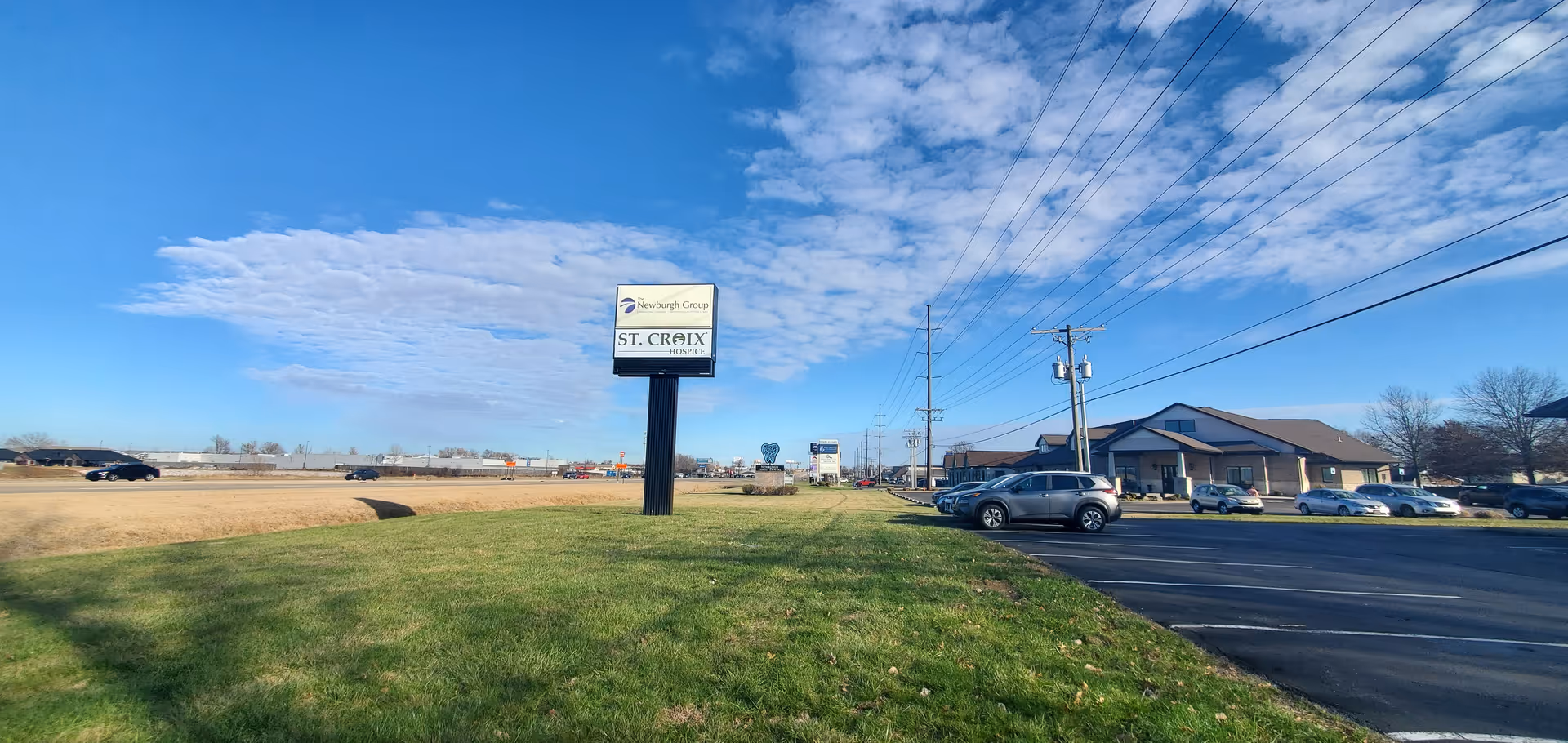 Wide exterior view of a St. Croix Hospice facility with sign, parking, and building.