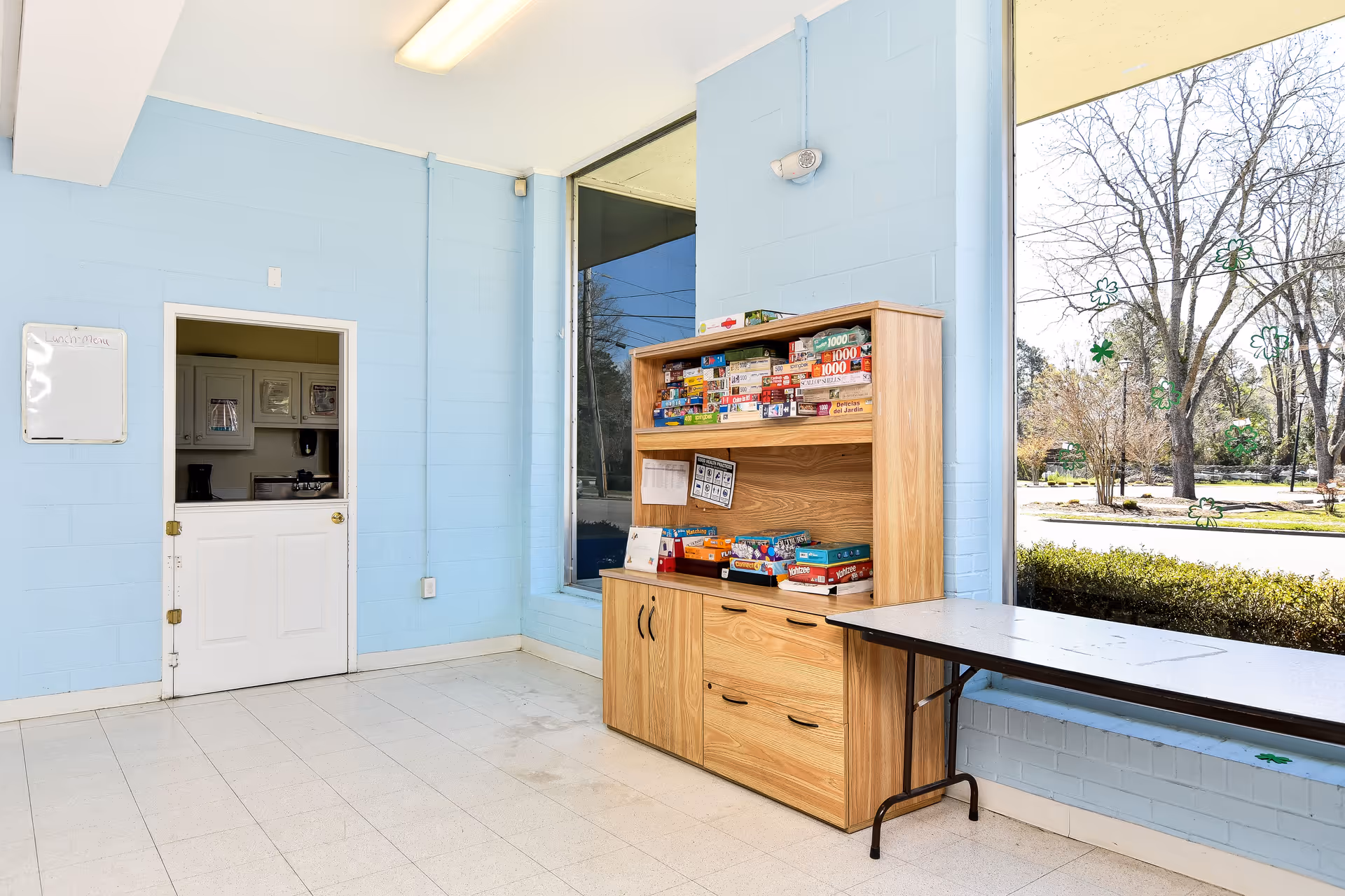Light blue interior with a kitchenette door, wooden game shelf, and a windowed table.