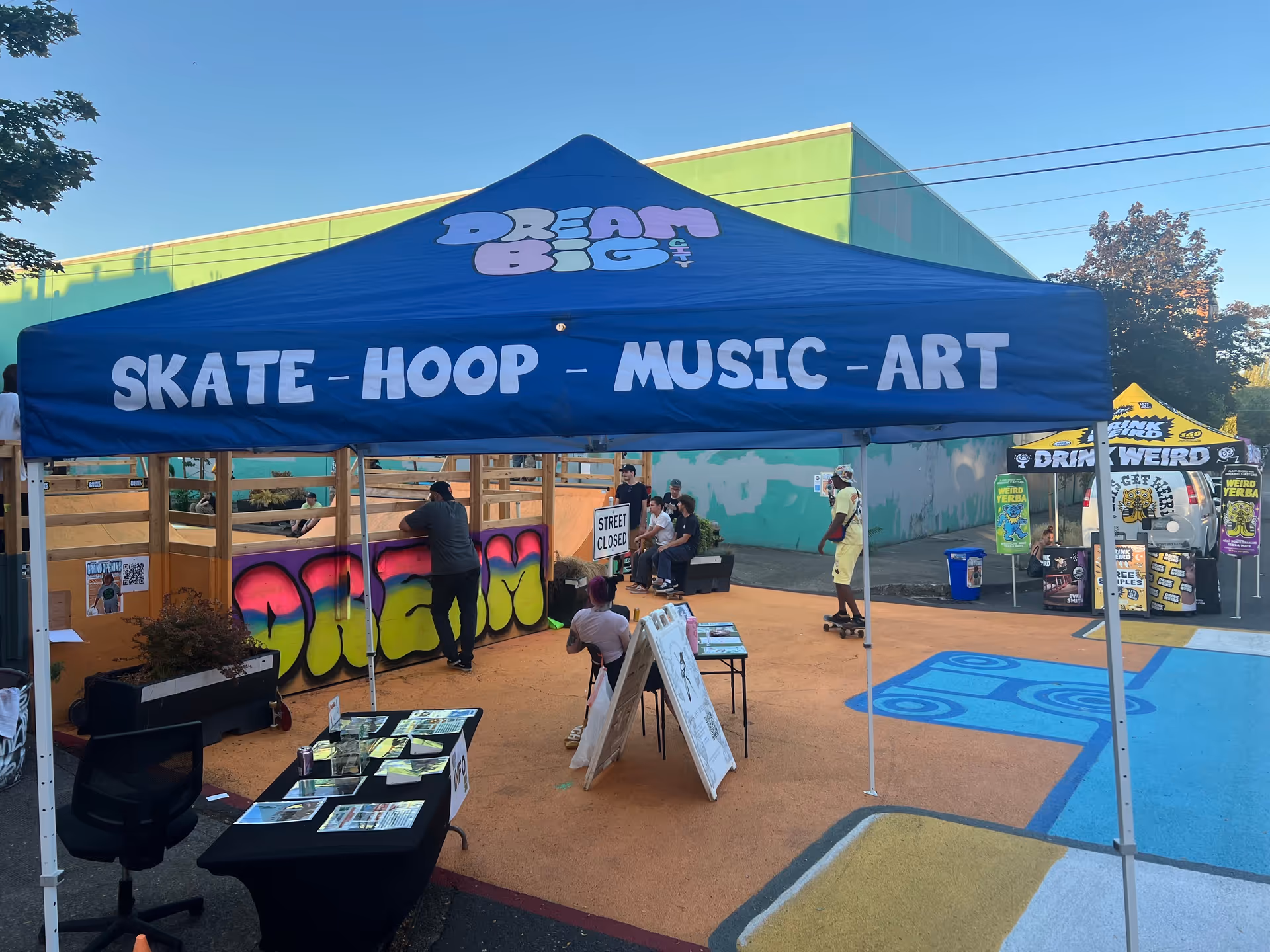 Blue canopy tent advertising Skate, Hoop, Music, Art at an outdoor event.