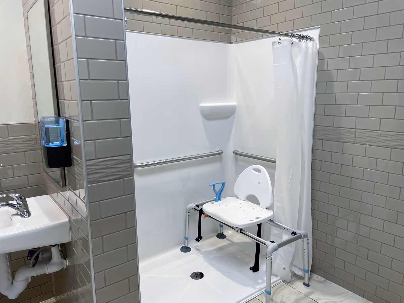 Accessible shower stall featuring a shower chair, grab bars, and a curtain.