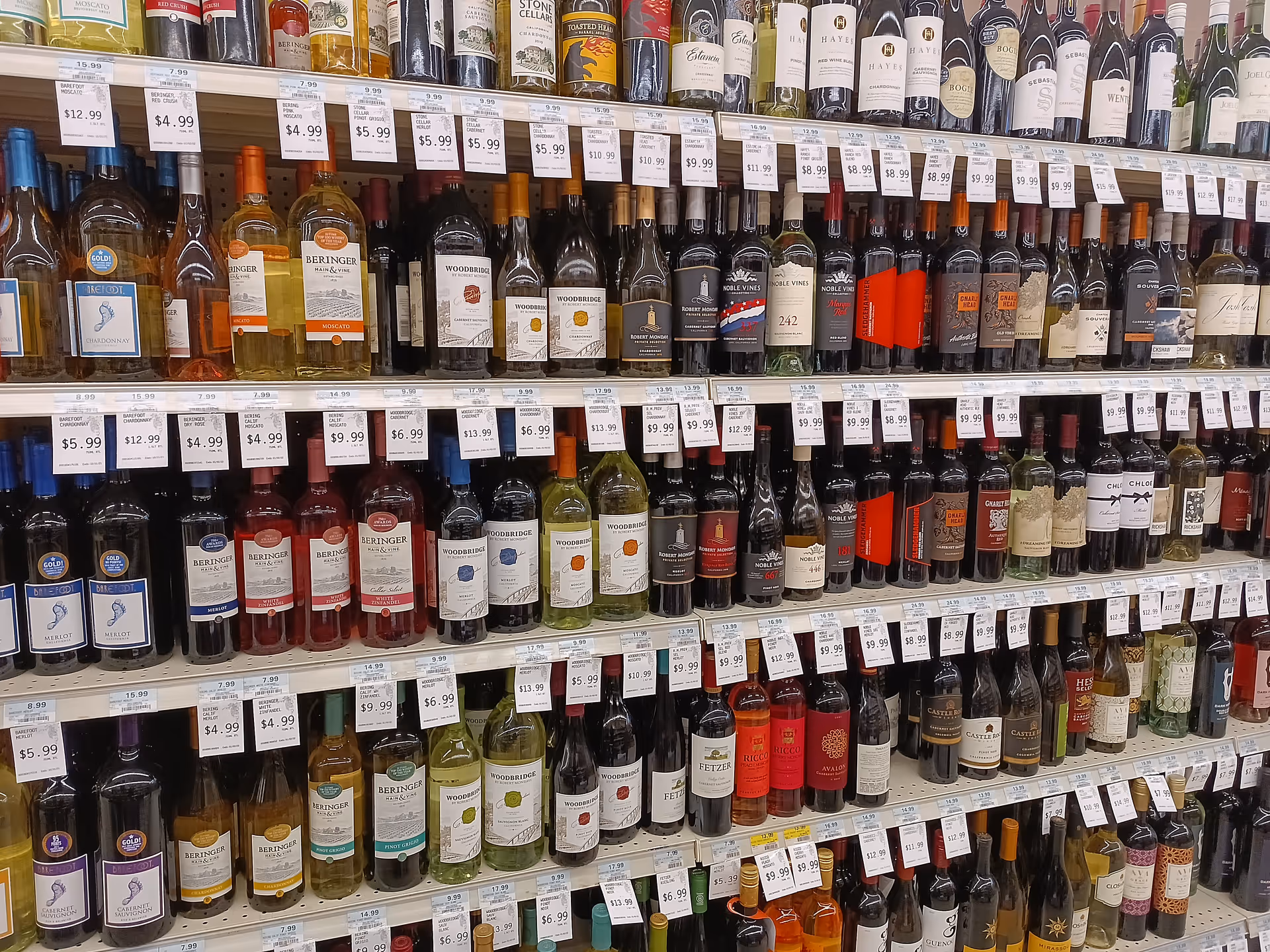 Rows of wine bottles lined on store shelves with price tags and labels.