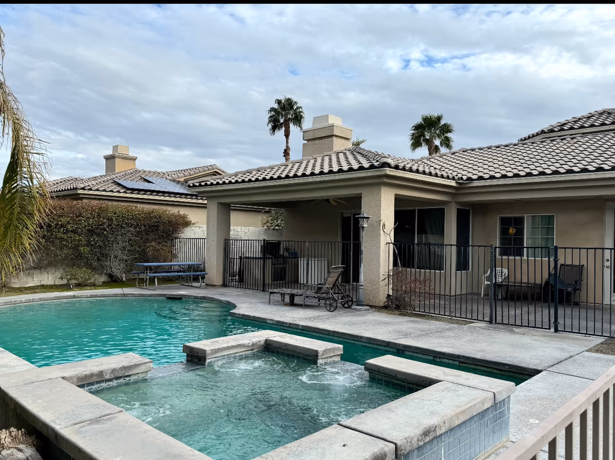 Outdoor pool and spa area with a fenced patio beside a beige, single-story building.