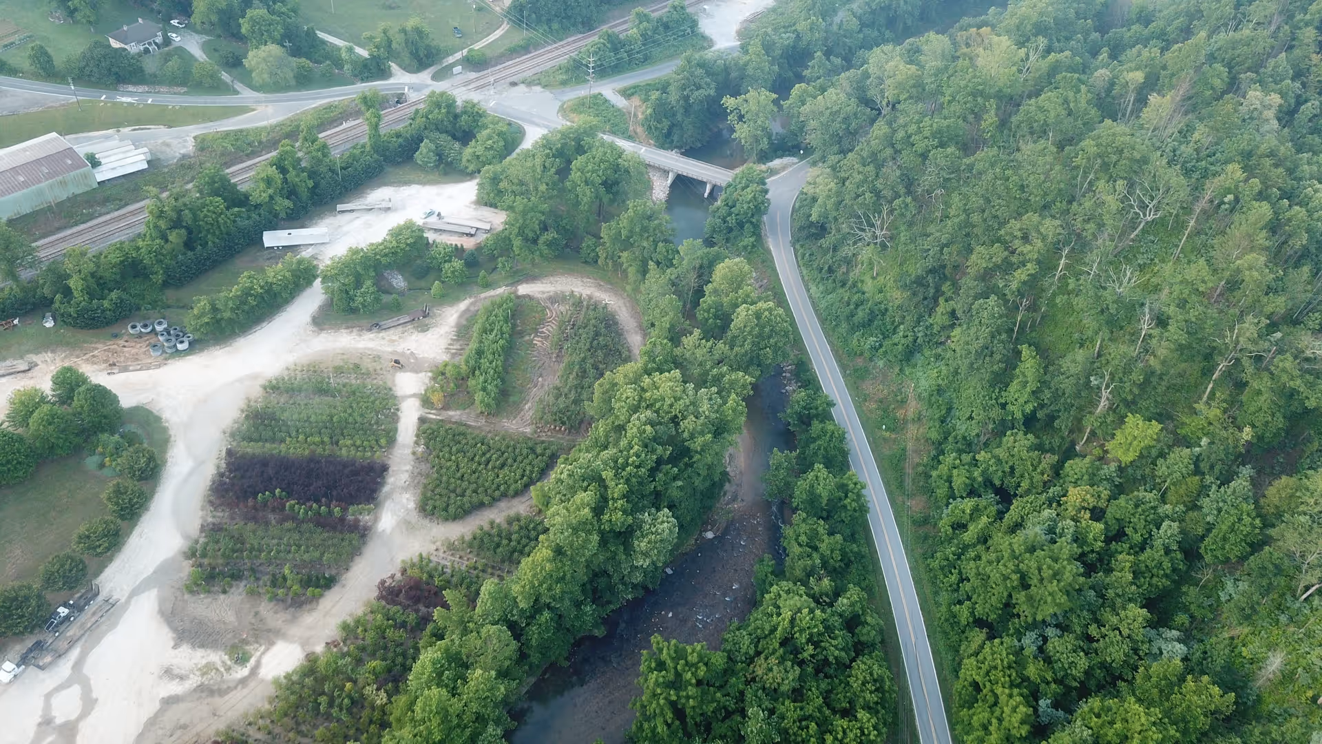 Aerial view of dense green landscape with winding road, river, and garden plots.