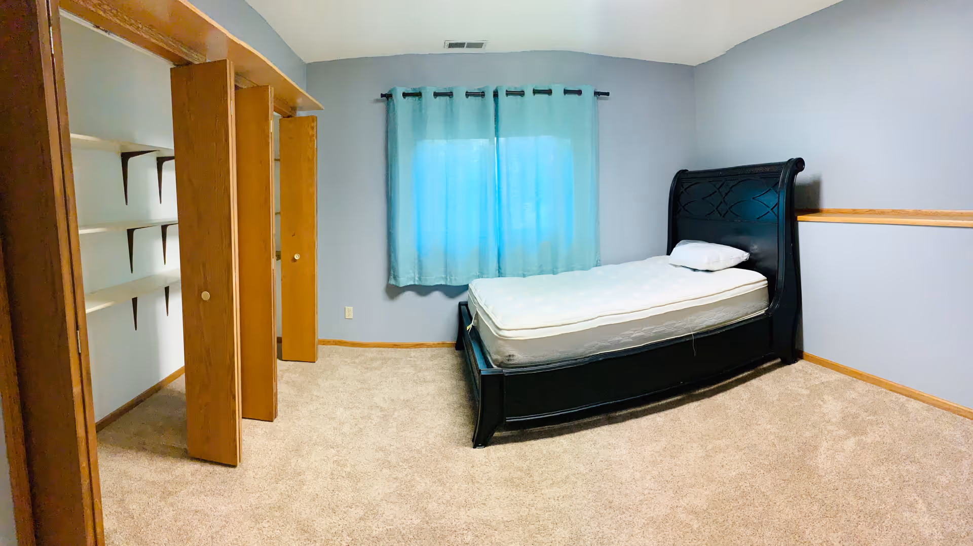 A bedroom with a black upholstered bed, open closets, and teal curtains.
