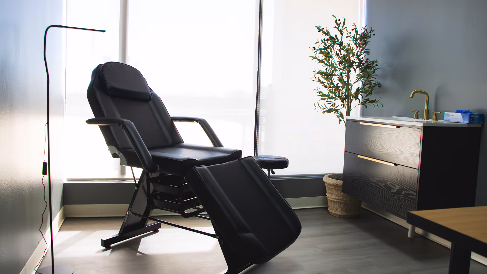 A black reclining chair in a bright therapy room beside a sink cabinet and plant.