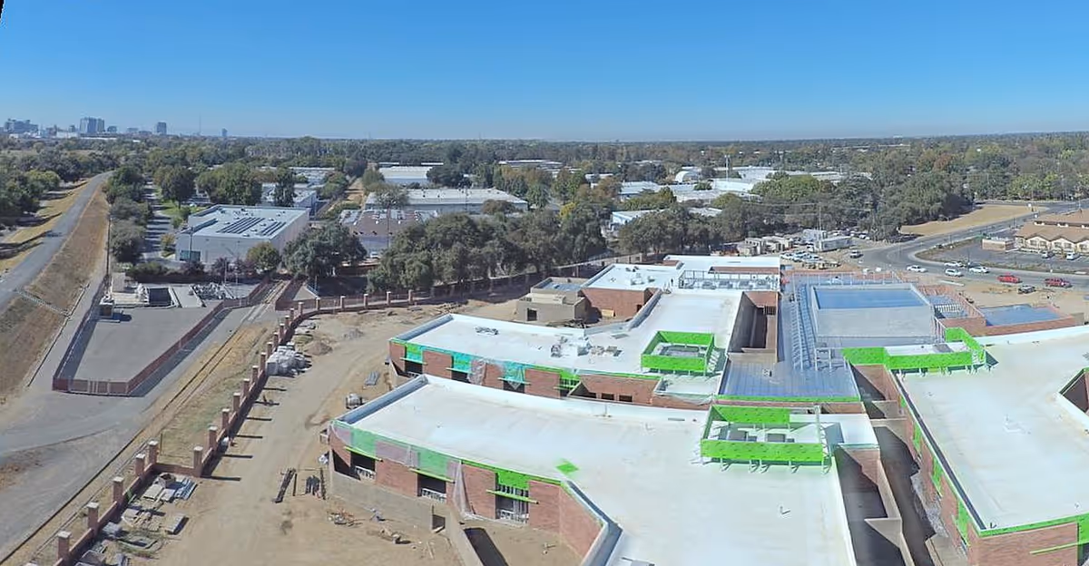Aerial view of a multi-building facility under construction with green rooftop coverings.