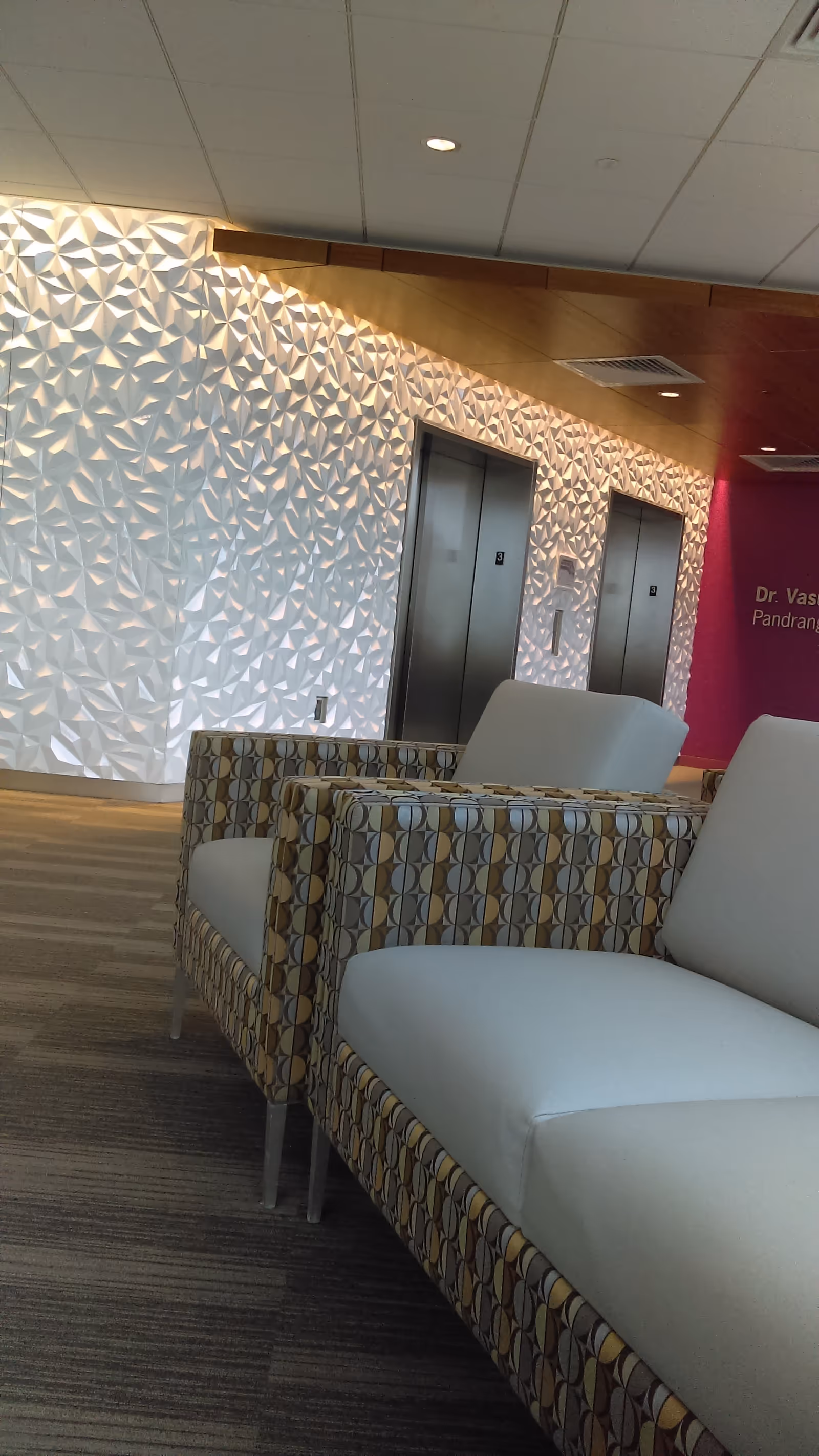 Lobby seating area with patterned walls, two elevators, and modern beige chairs.