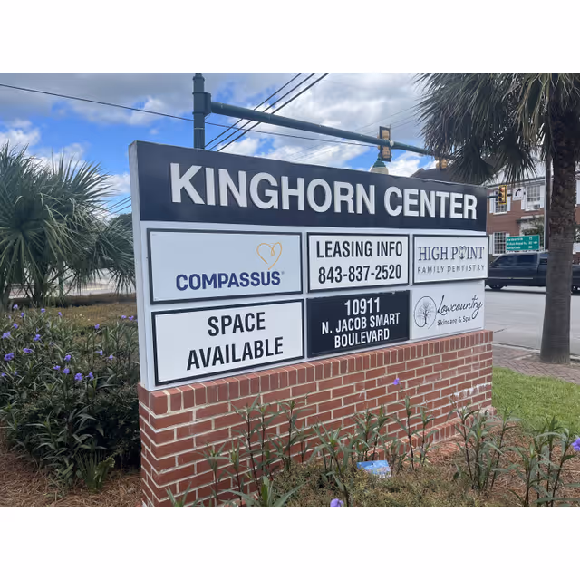 Exterior sign reading KINGHORN CENTER with COMPASSUS logos and leasing info, brick base, landscaping.