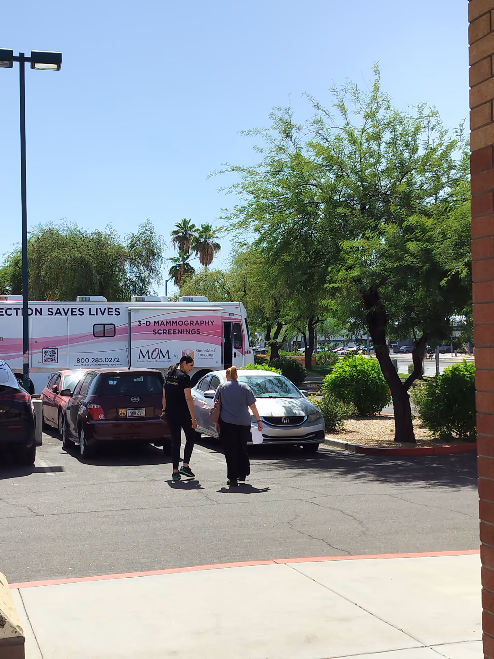 Exterior parking lot of MY DR NOW with a pink mammography van and pedestrians.