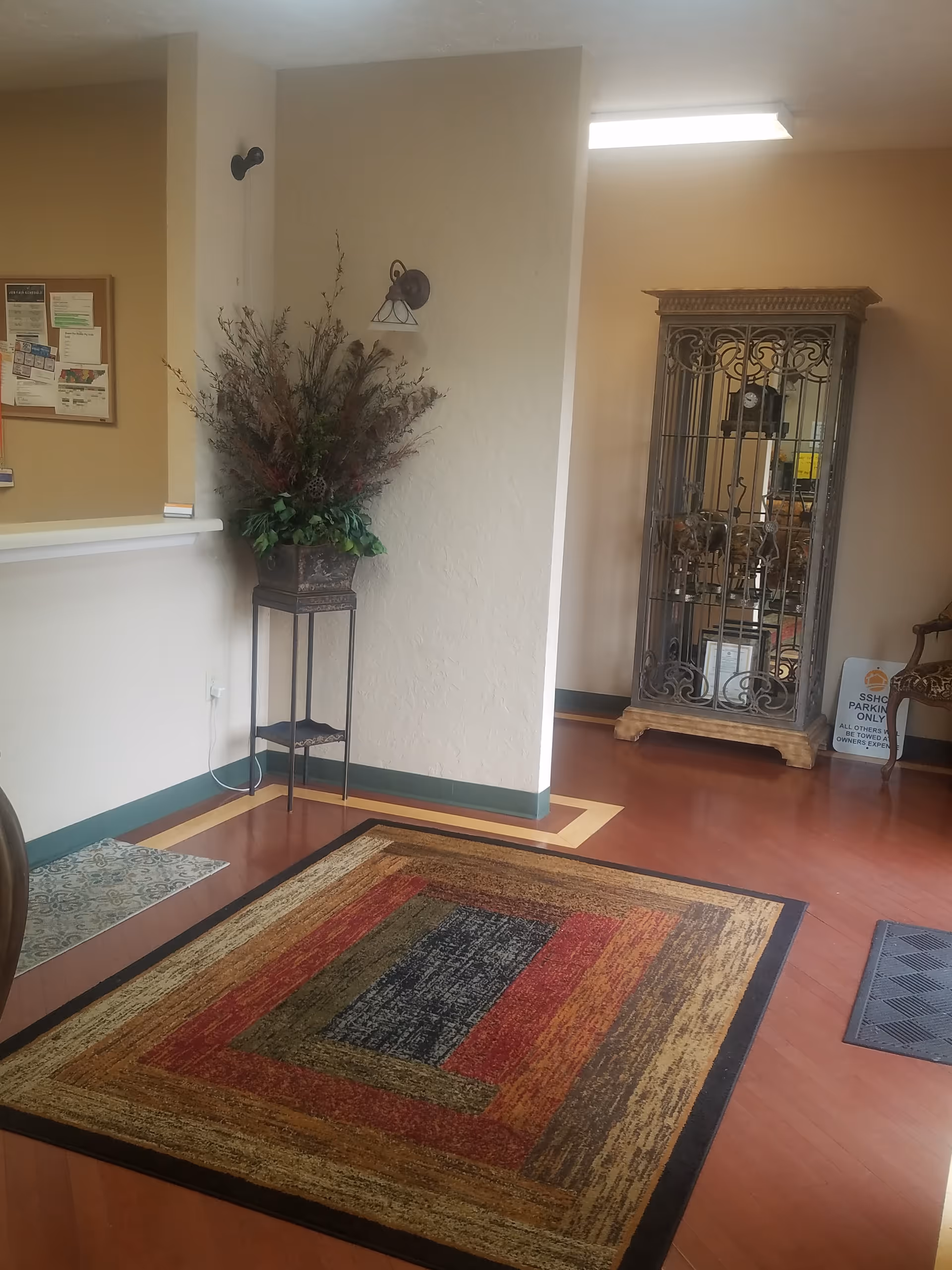 Interior lobby of a senior living facility with rug, pillar, plant display, and cabinet.