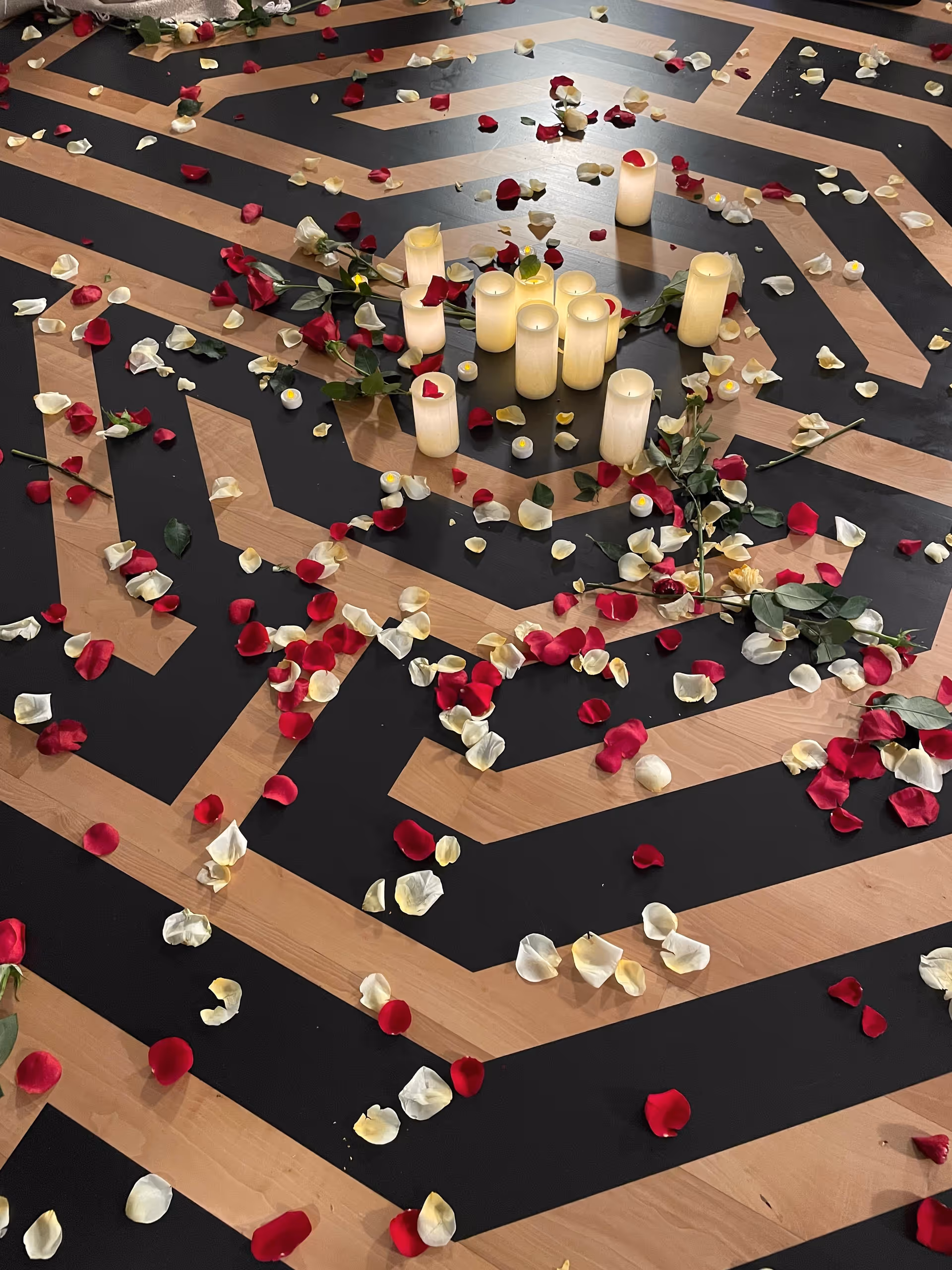 Candles and rose petals arranged on a geometric indoor floor.