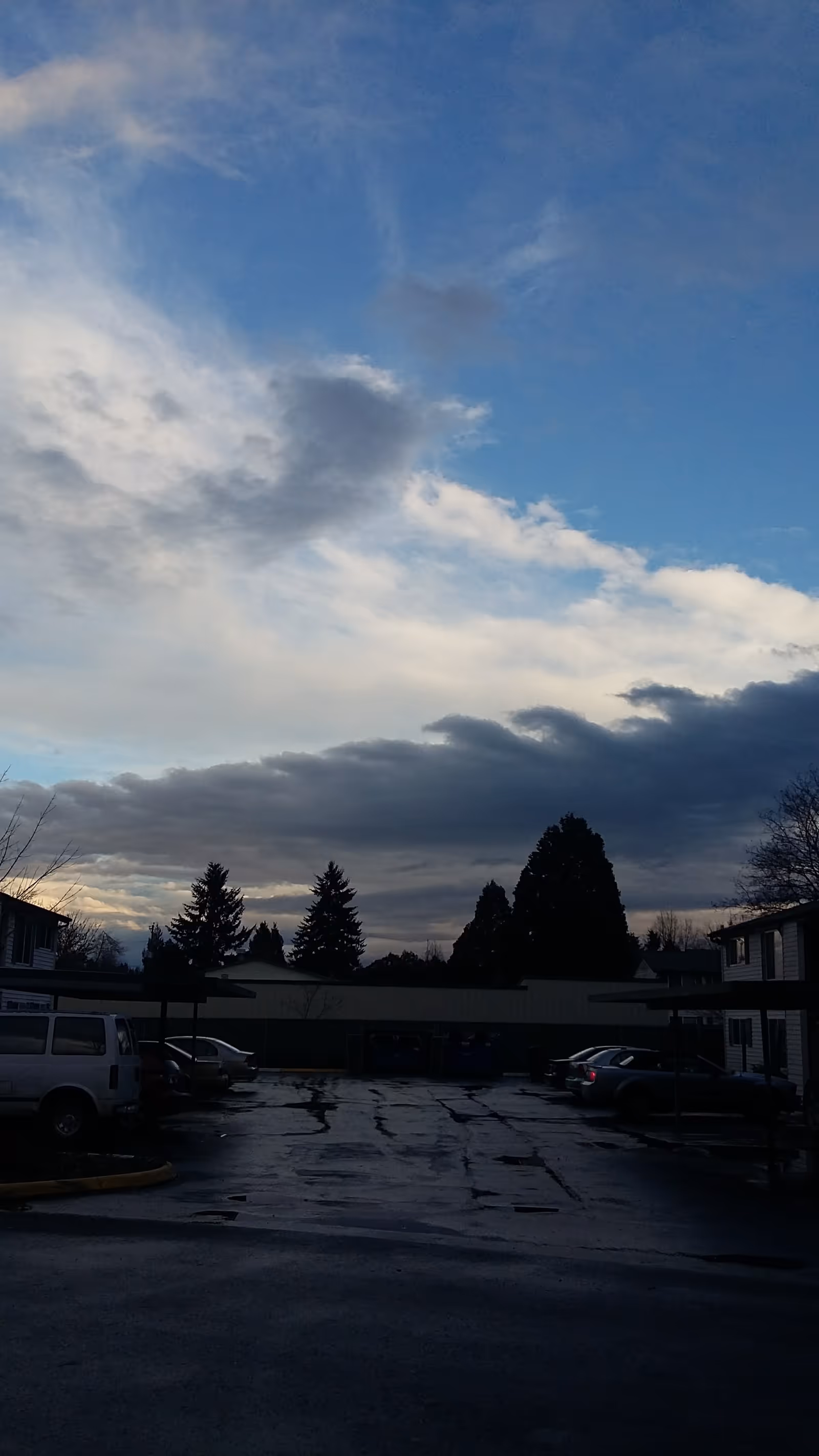 Exterior view of a senior home parking lot with trees and a cloudy sky.