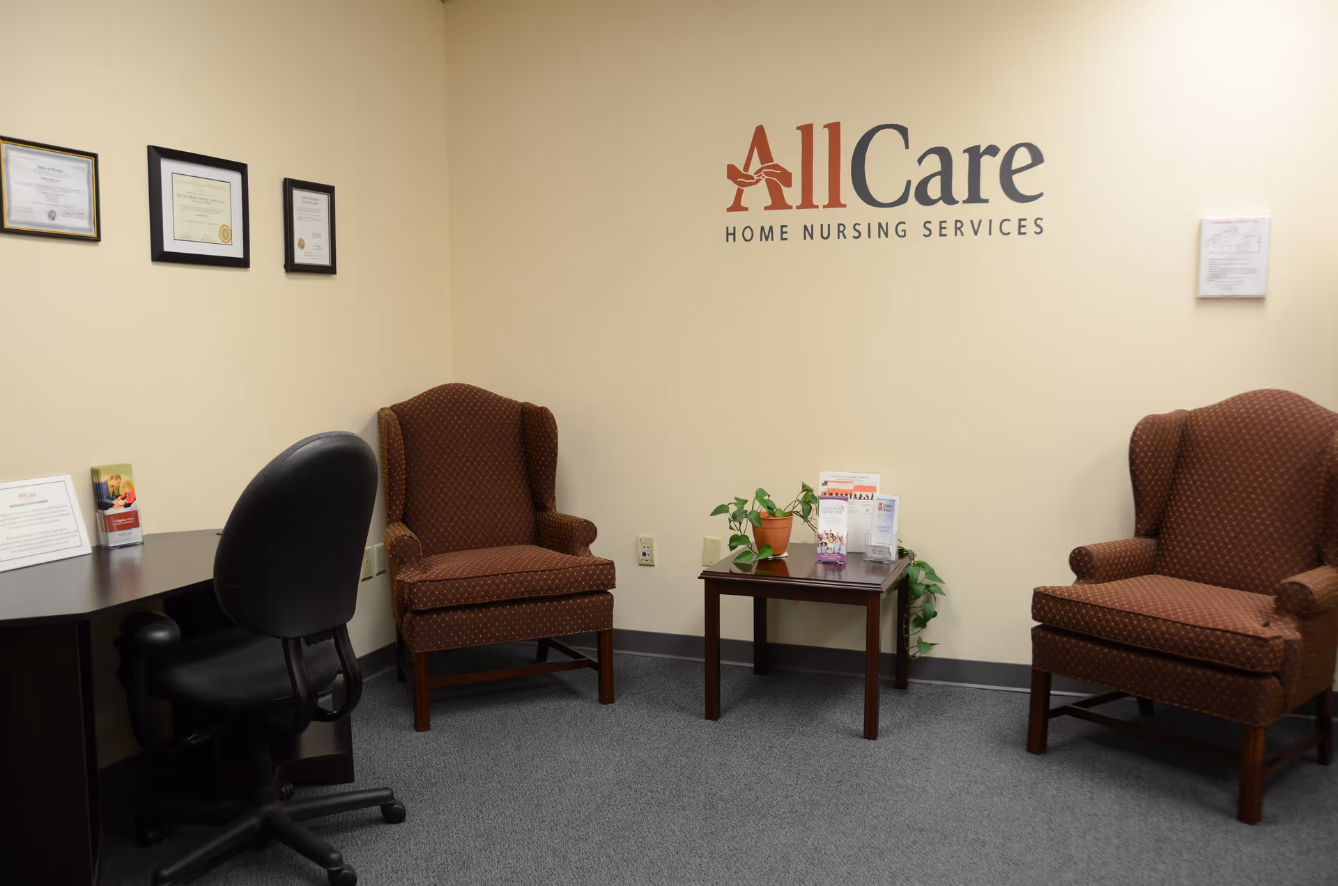 Reception area with two brown armchairs, a small table with plants and brochures, wall logo.