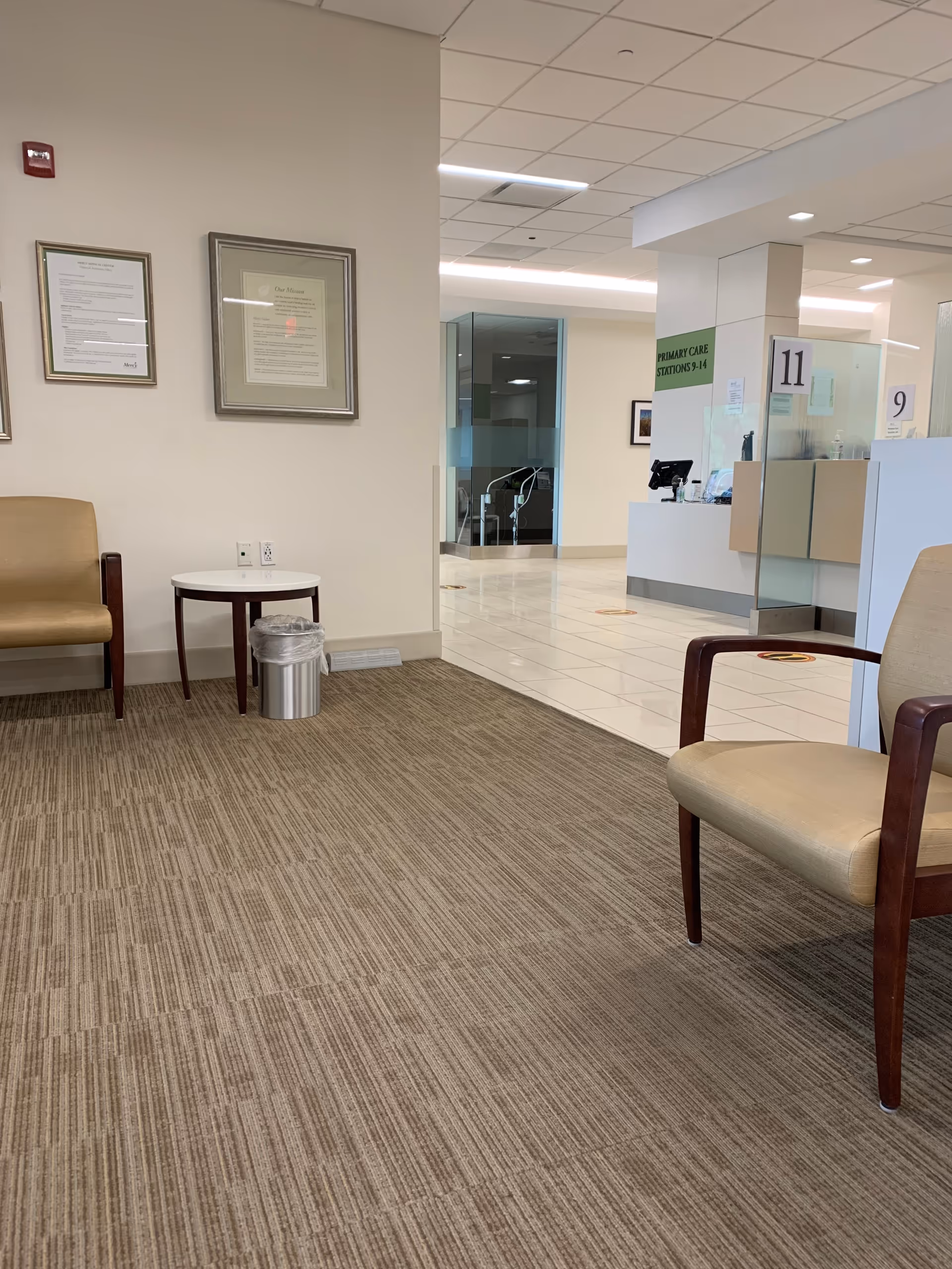 Empty medical lobby with beige chairs, small side table, framed certificates