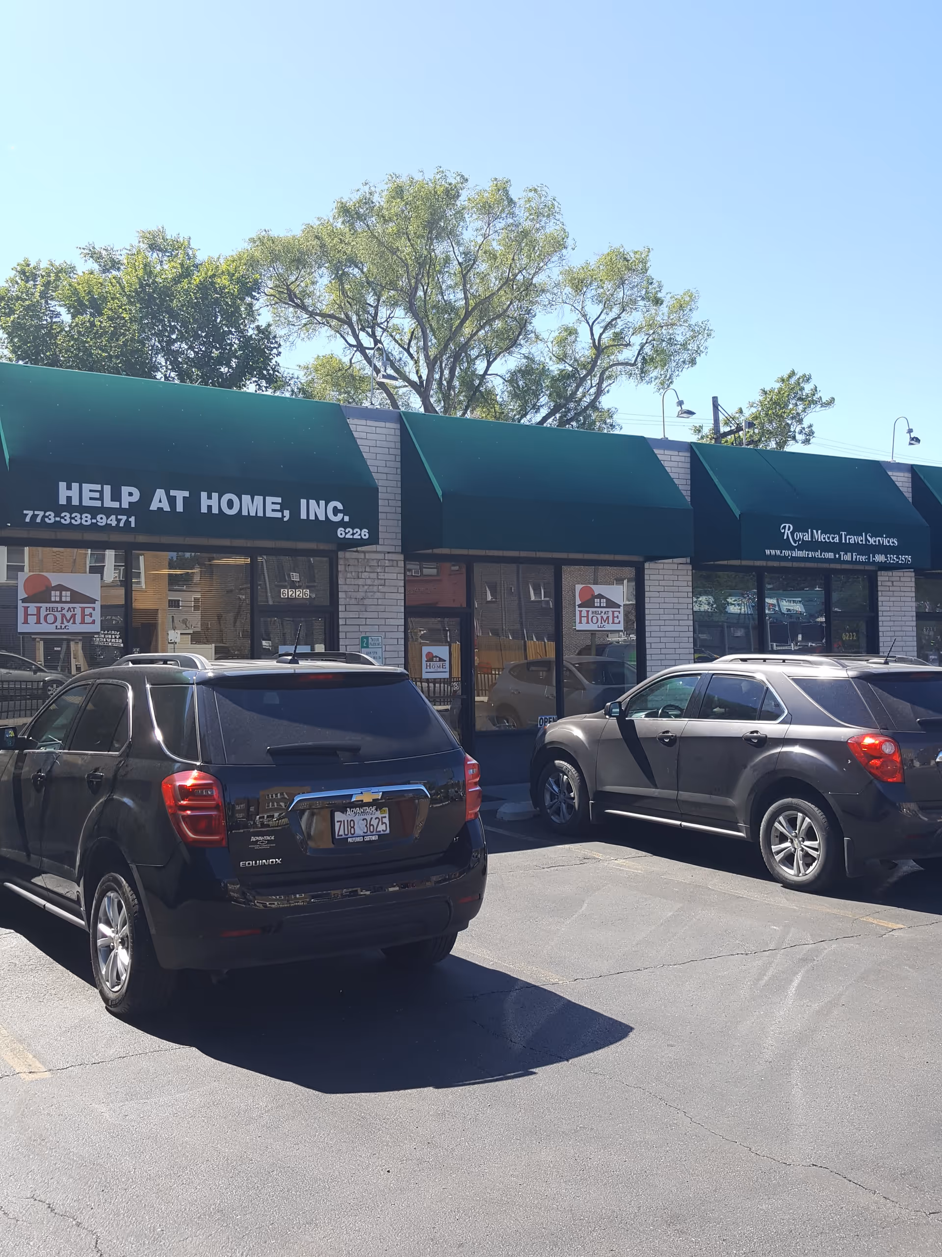 Front view of Help at Home storefronts with green awnings and several parked cars.