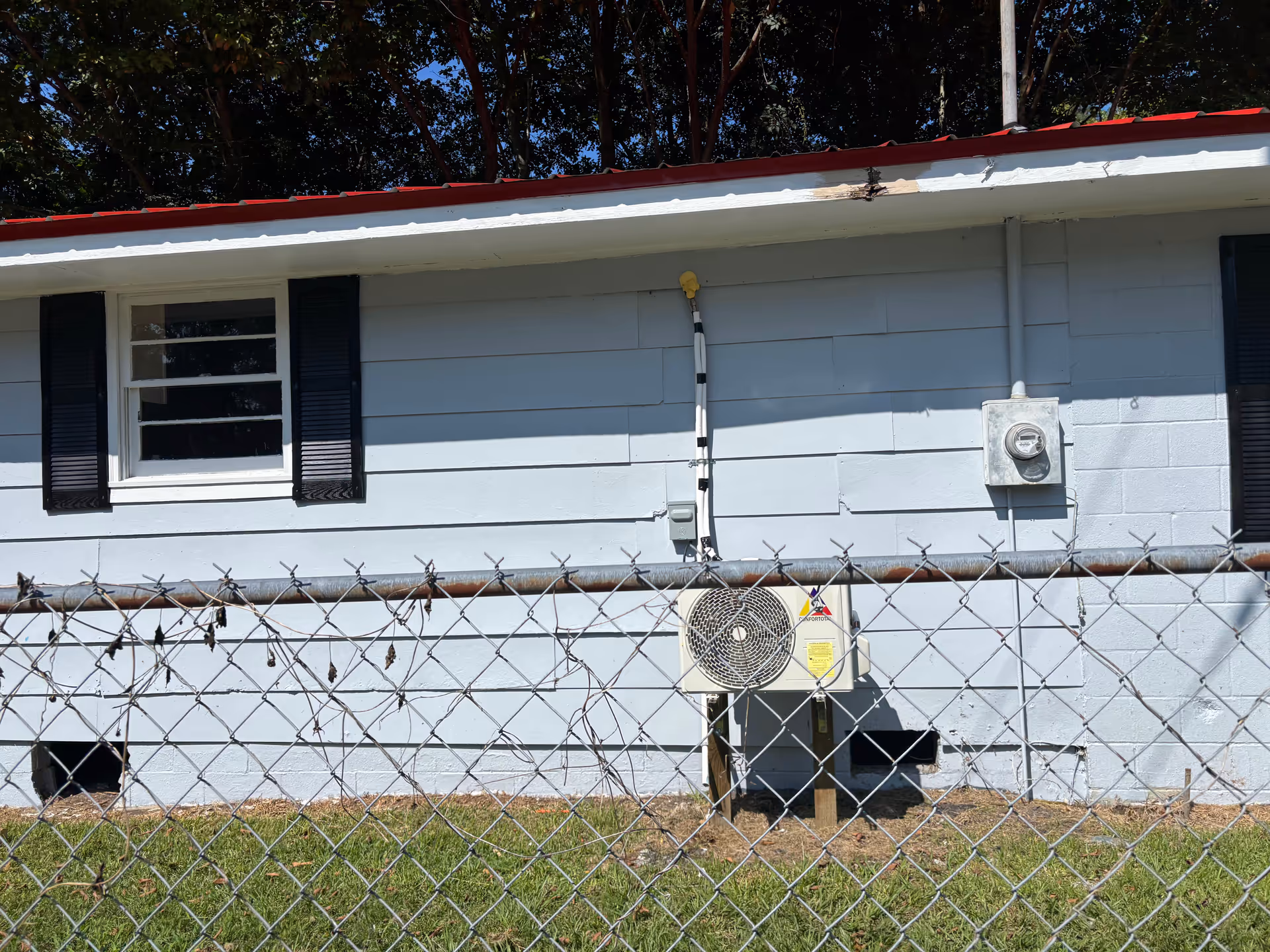 Side of a light-gray single-story building with a chain-link fence and utility meters.