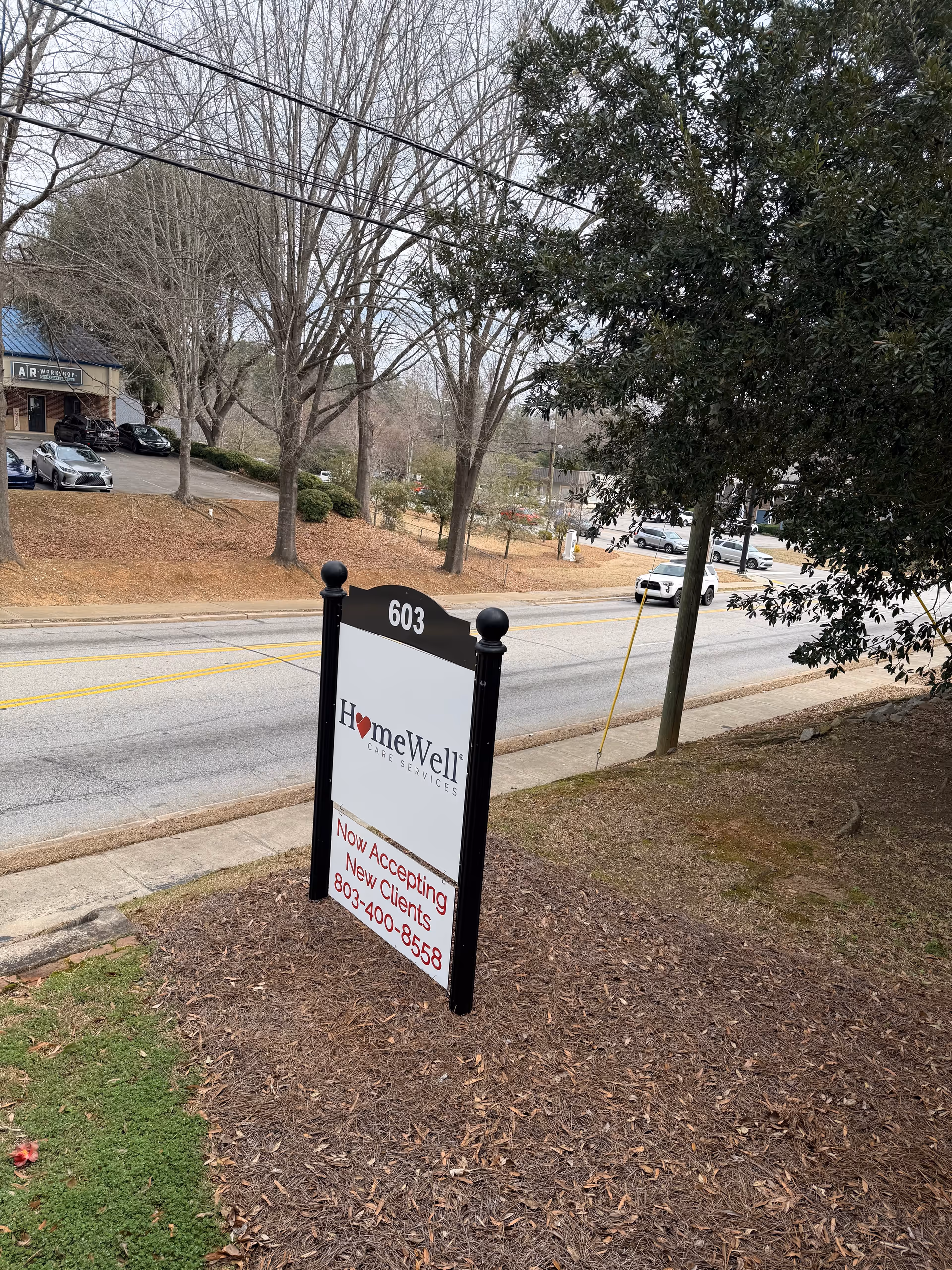 Exterior street scene with a HomeWell Care Services sign near a road and trees
