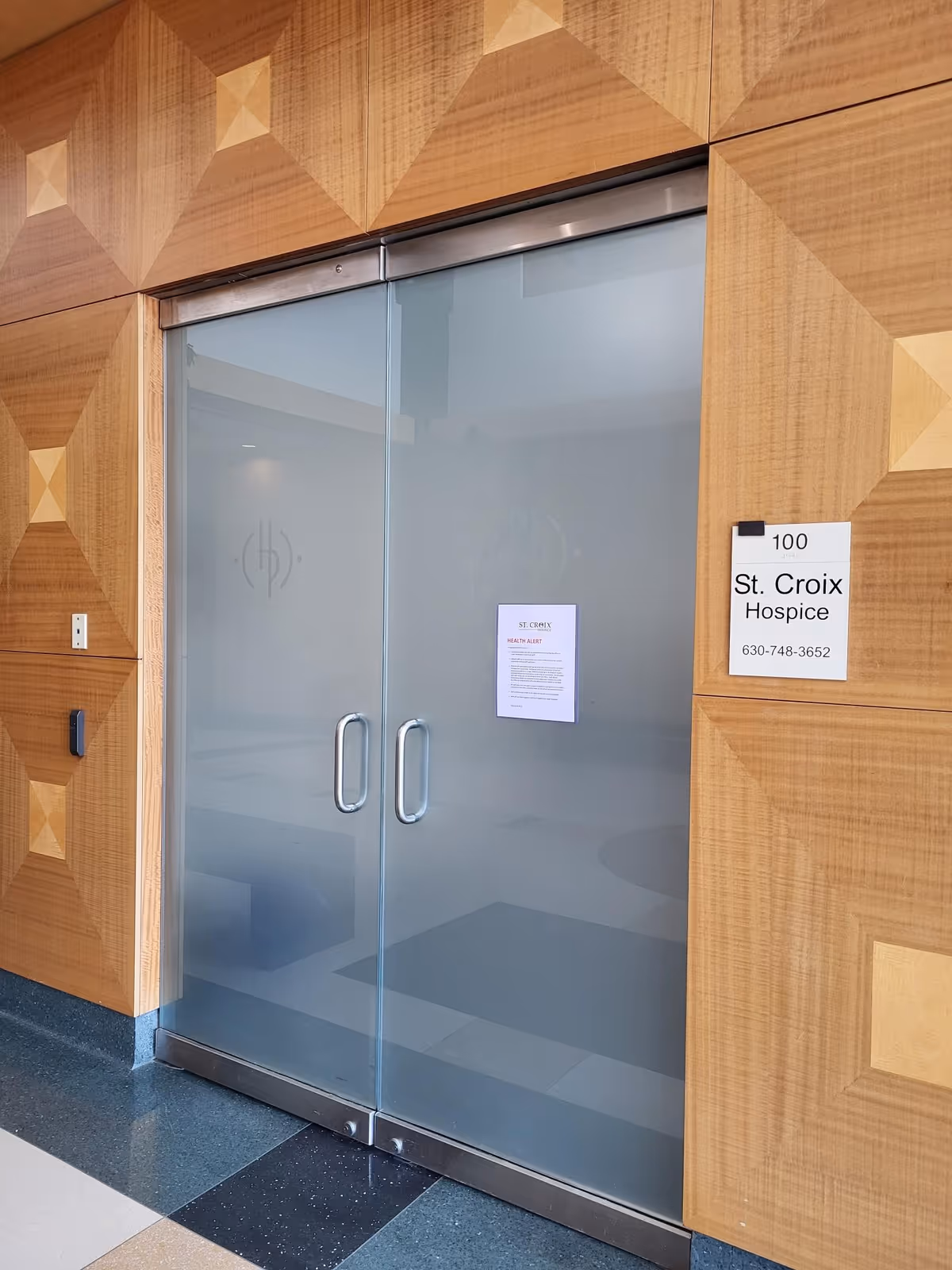 Double glass doors framed by wood panels with St. Croix Hospice sign nearby.