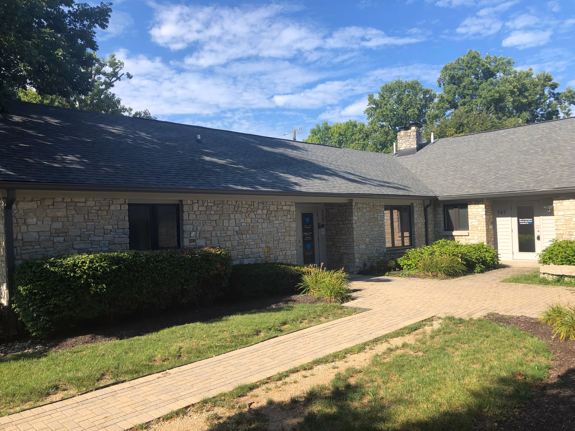 Stone building exterior with a brick walkway and green shrubs around the entrance.
