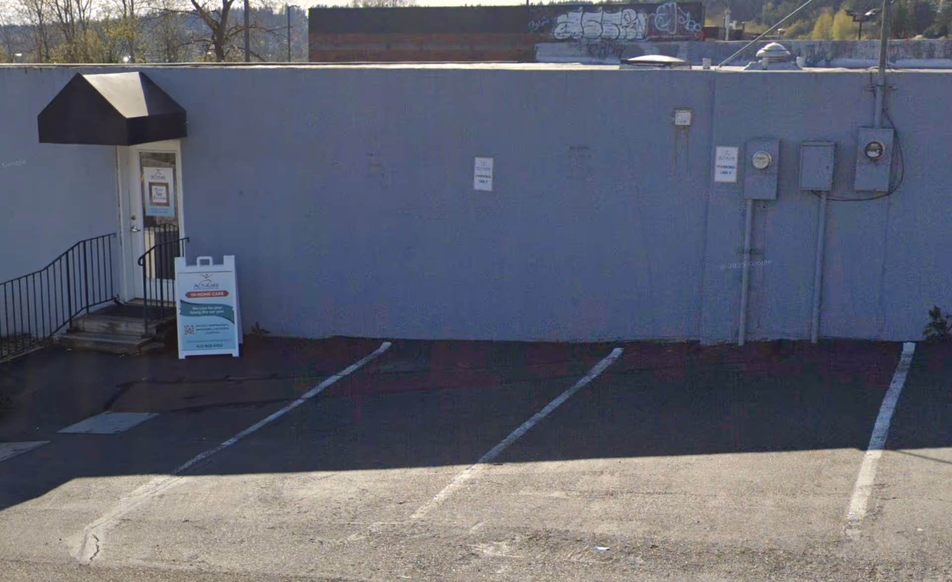 Exterior wall of a building with a door, awning, and a parking lot.