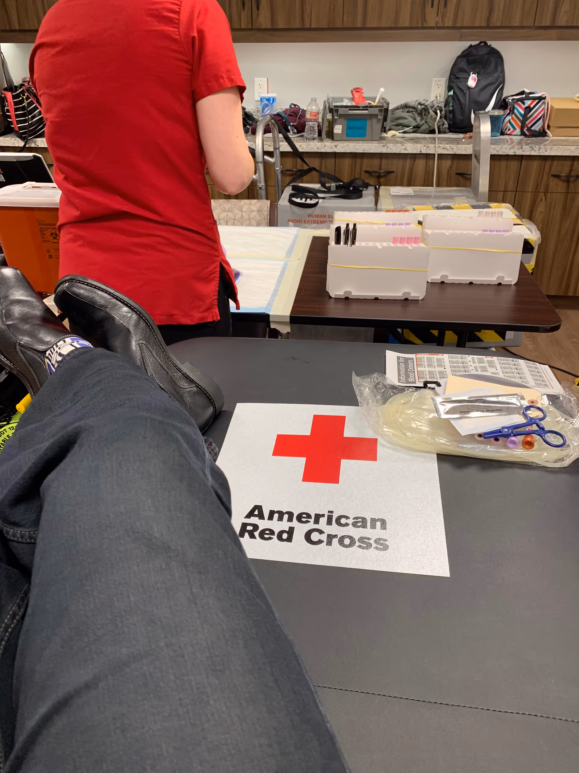 Person in red shirt at a medical supply counter with Red Cross logo on the table.