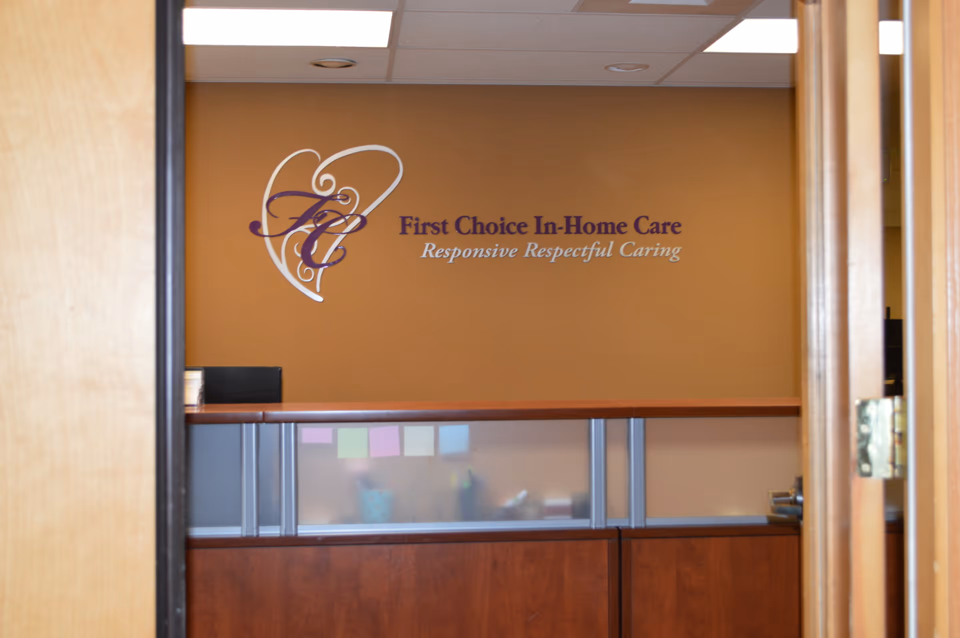 Reception desk with logo on a brown wall inside a First Choice In-Home Care office.