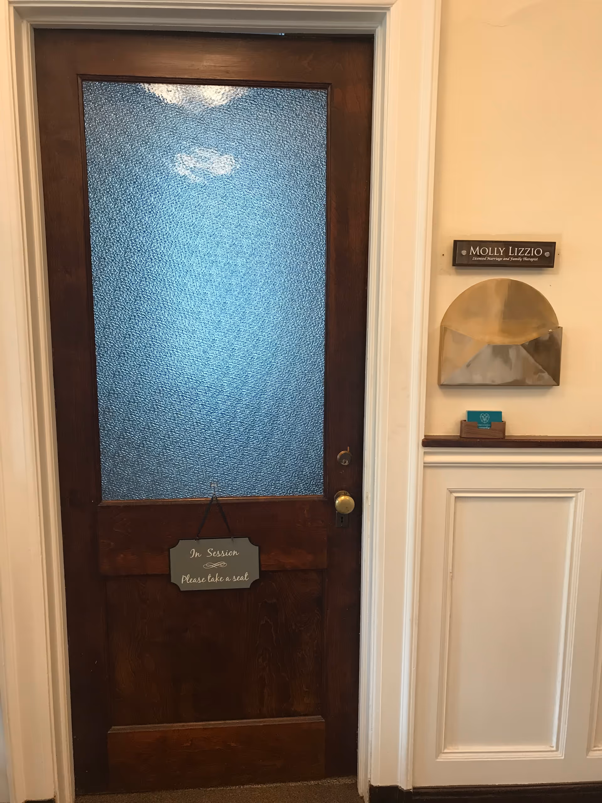Wooden door in a hallway with frosted glass panel and an 'In Session' sign.