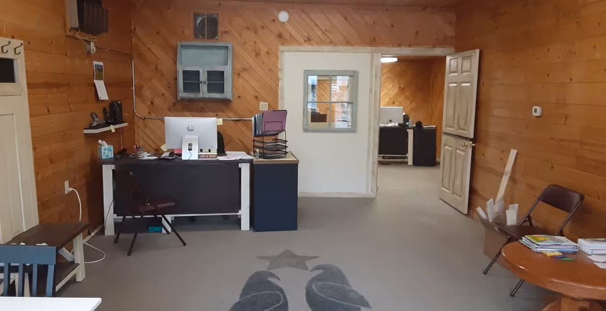 Wood-paneled office area with desks, computers, chairs, and a doorway to another room.