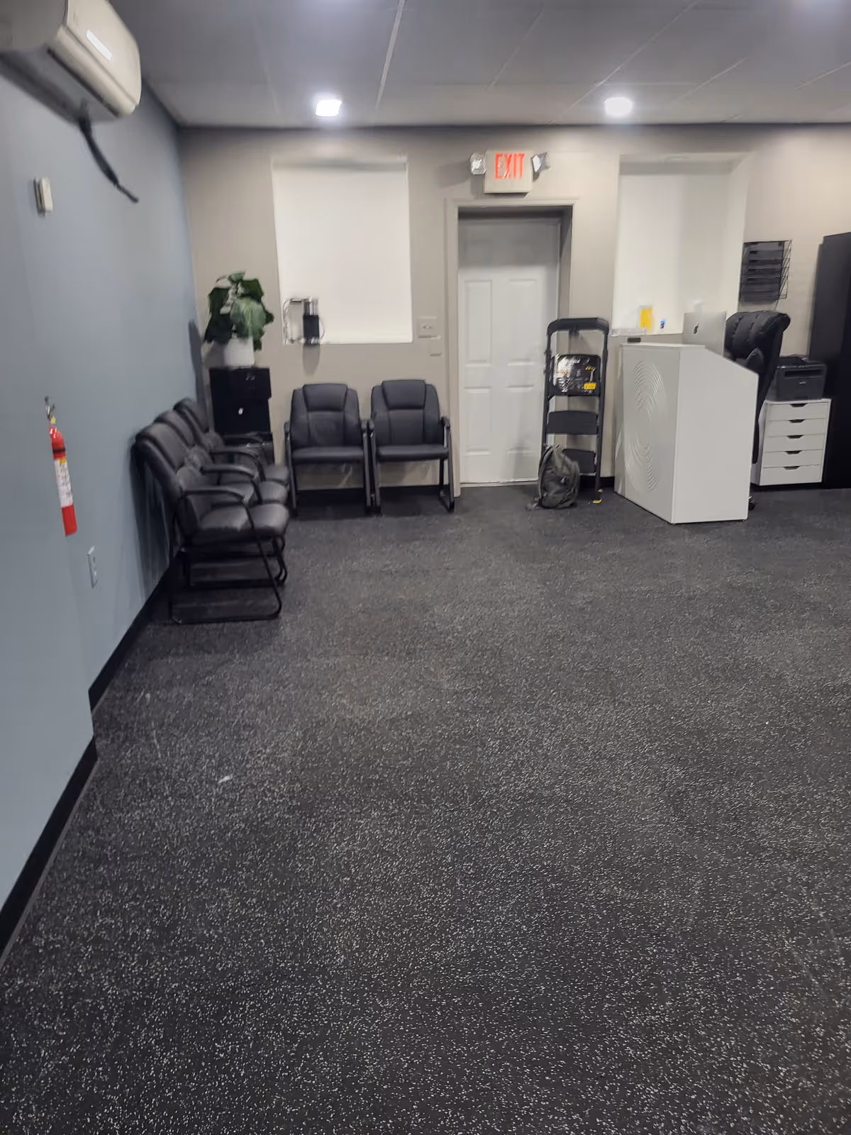 A quiet interior waiting area with black chairs, a doorway, and a white reception desk.